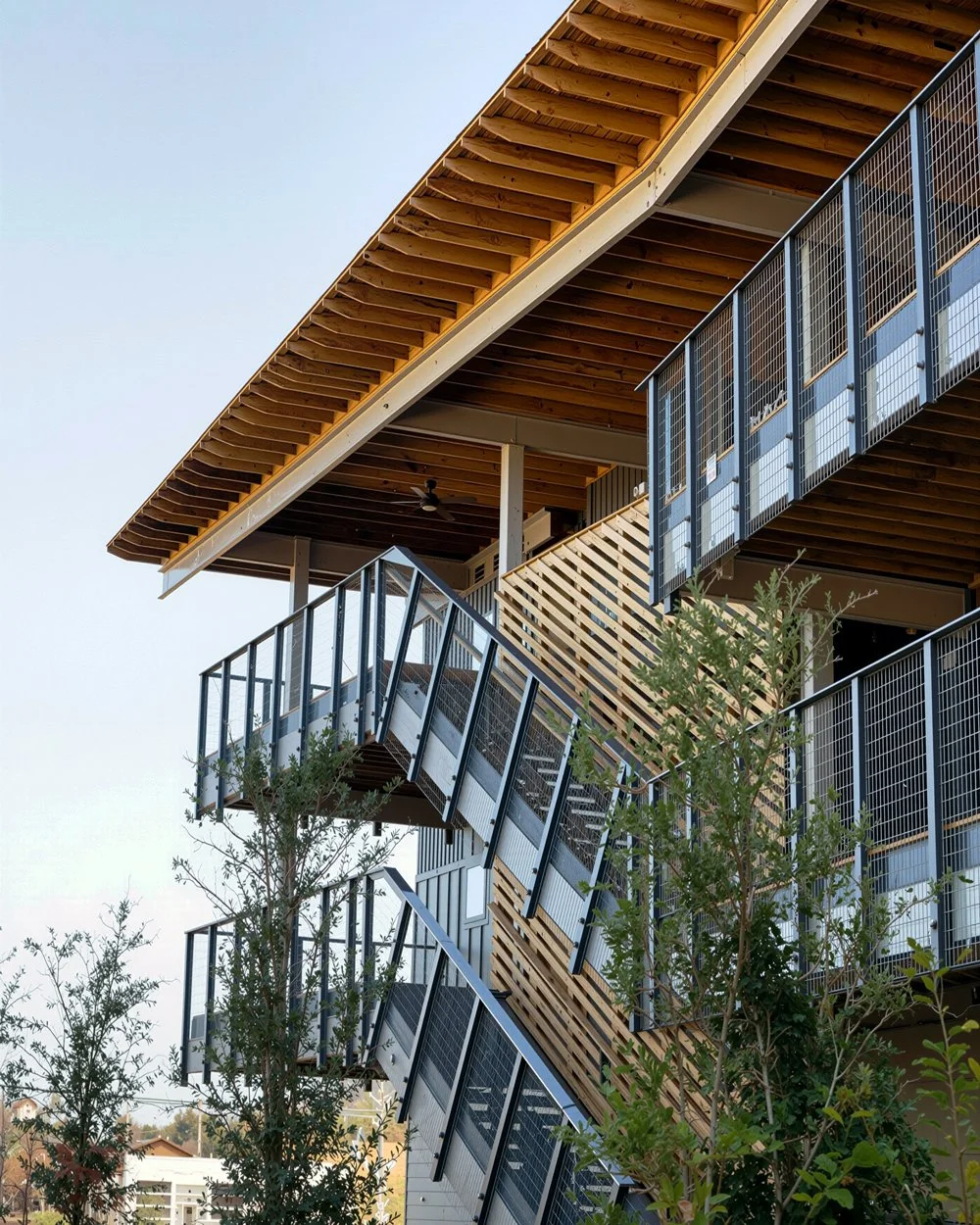 Exterior view of a modern multi-story building with wooden overhangs and metal staircases.