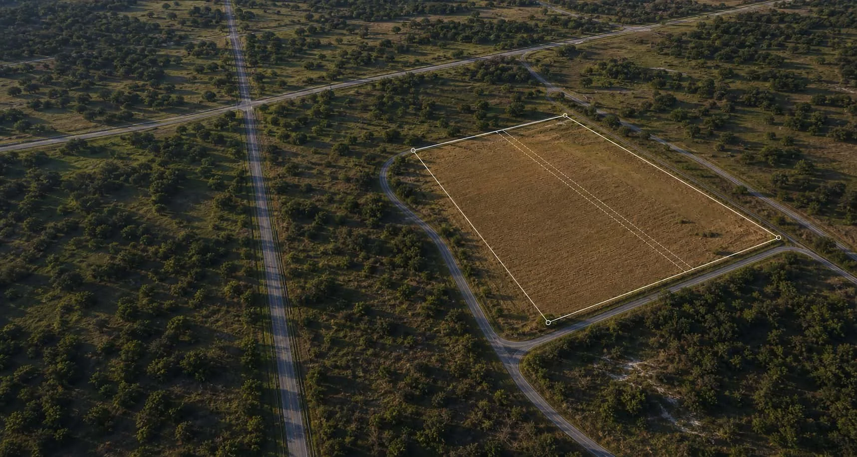 Aerial view of a large rectangular plot of land outlined with lines, surrounded by trees and roads in a rural area.