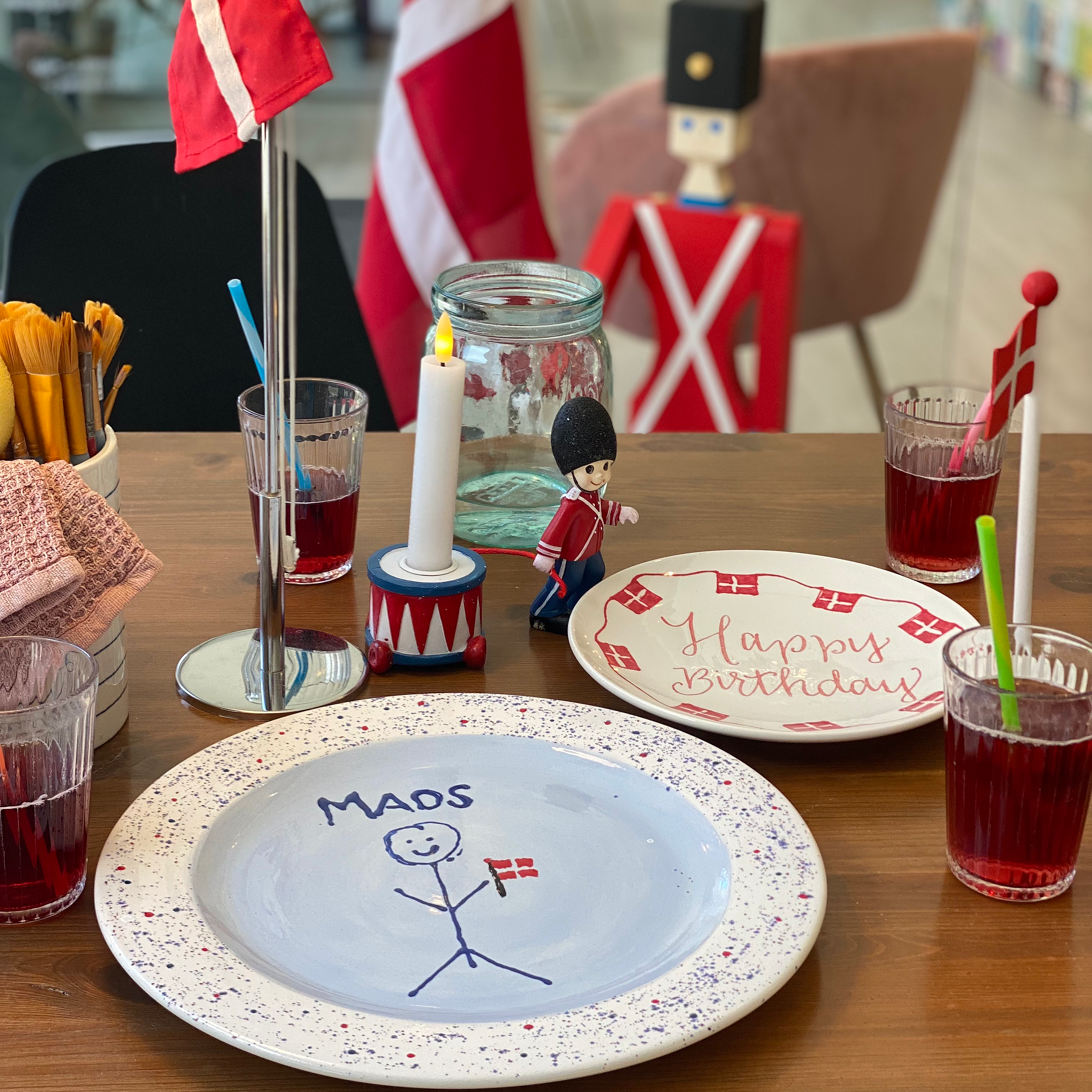 En tallerken med en tegning af en glad person, der holder en dansk flag. Tallkens tekst siger 'Happy Birthday'.