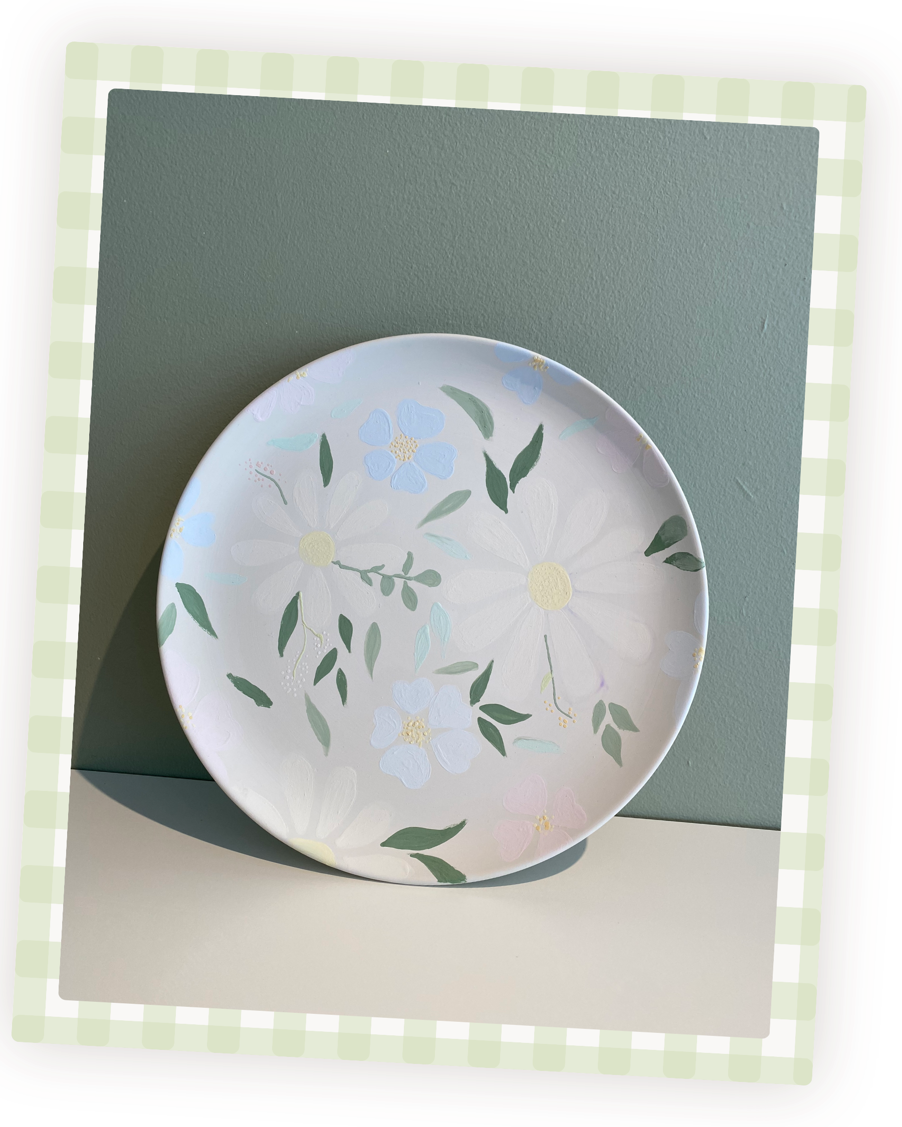 En hvid keramisk tallerken med pastelfarvede blomster- og bladmotiver, placeret på en anden større grøn plade eller underlag.