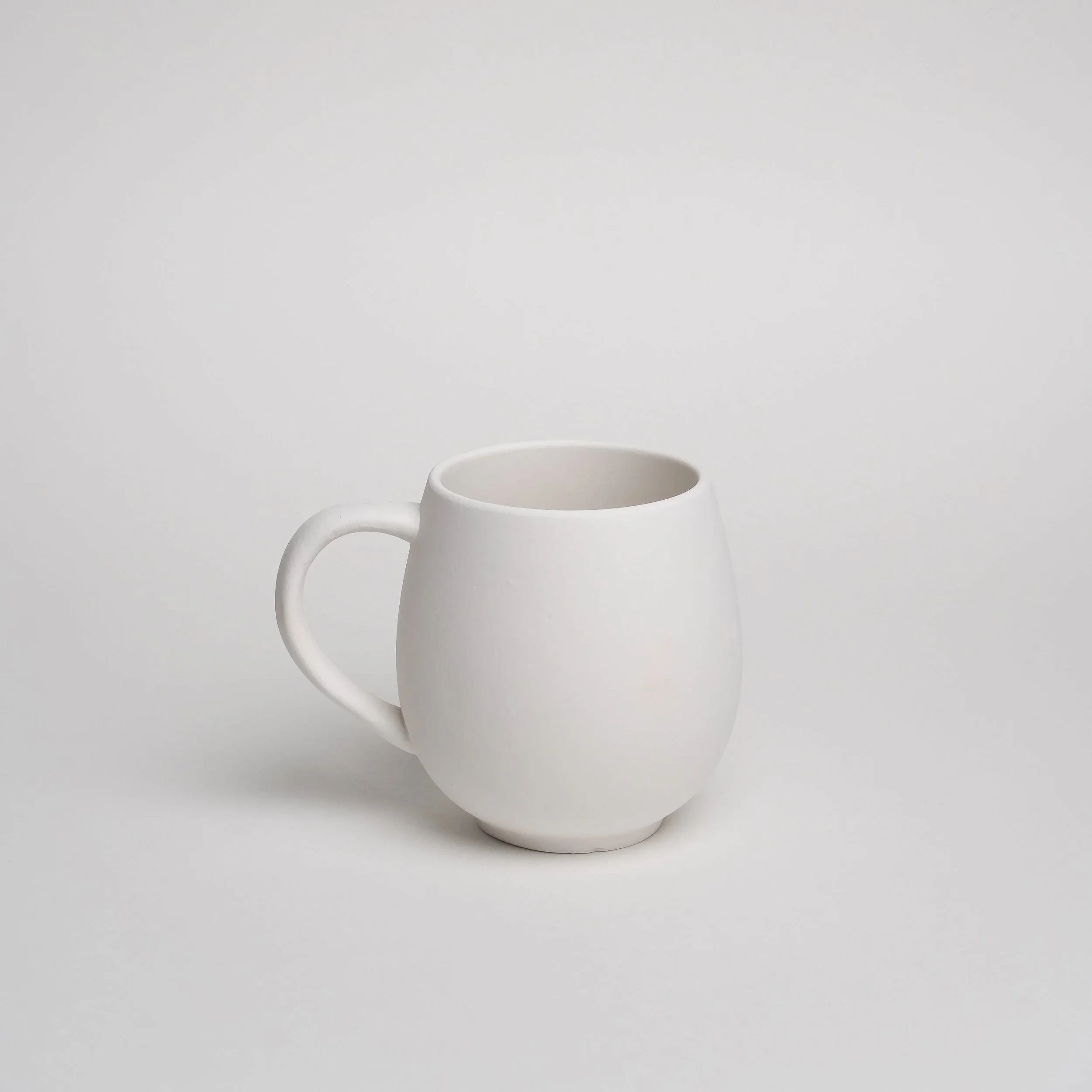 Hvid keramikmug på en hvid overflade med en blank baggrund.