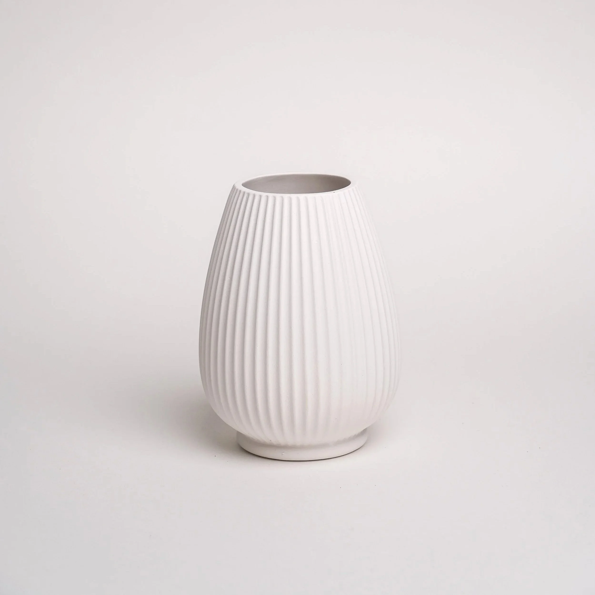Hvid, ribbet, keramisk vase med en bred åbning på toppen og en smal bund.