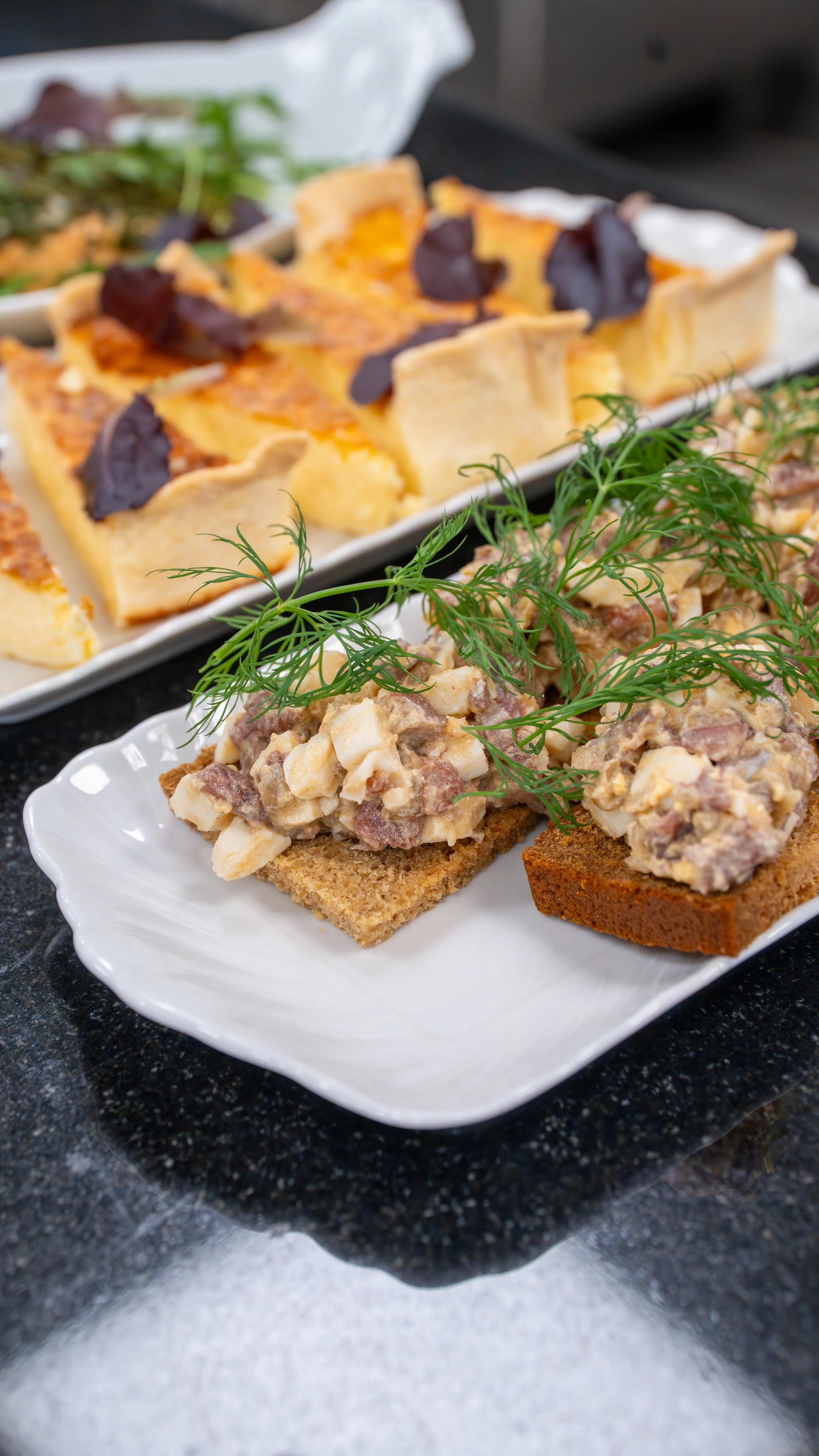 Appetizer platter with cheese and prosciutto, topped with herbs and garnishes.