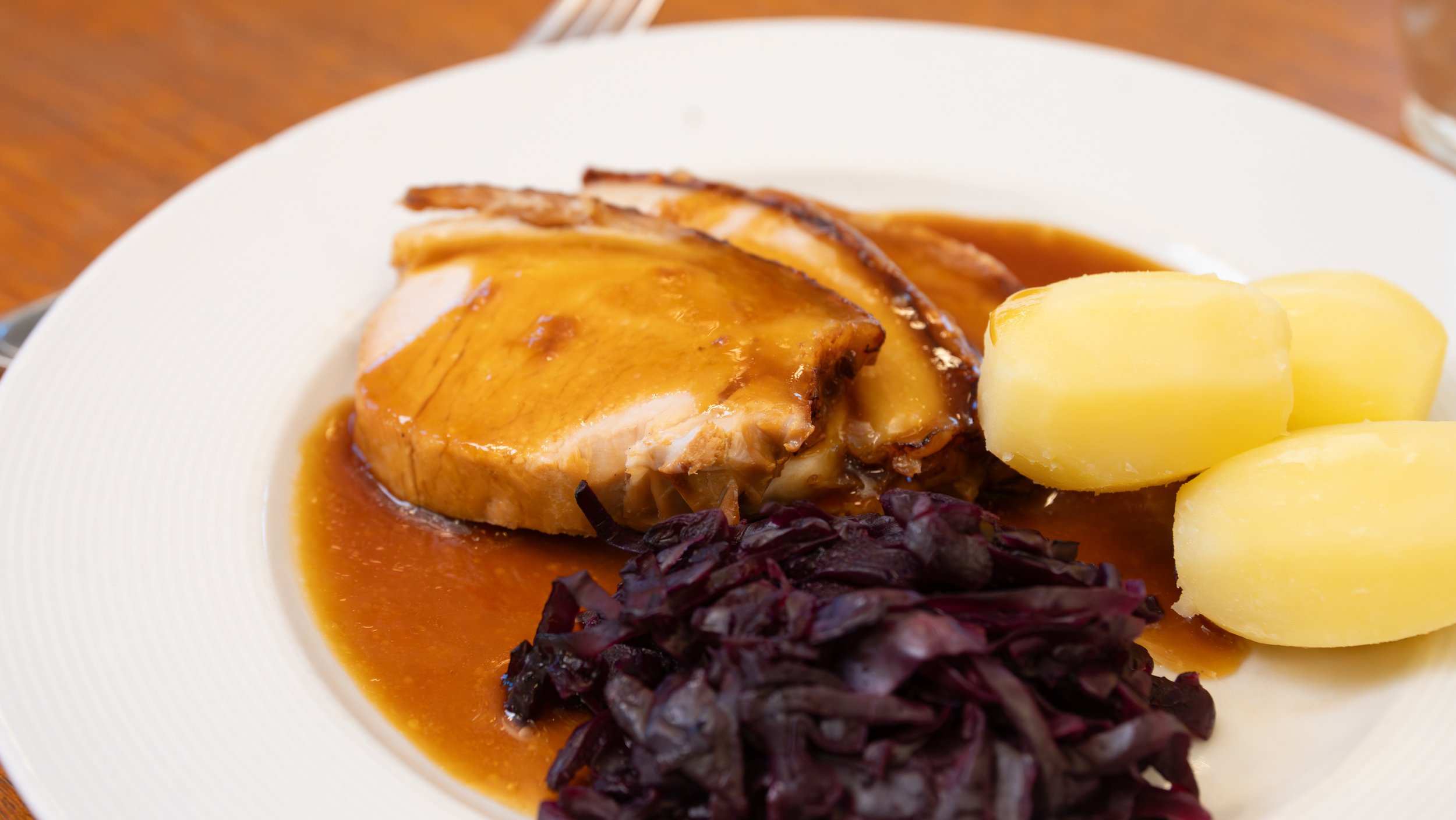 A plate of food with a piece of cooked chicken topped with gravy, boiled potatoes, and a serving of cooked red cabbage.