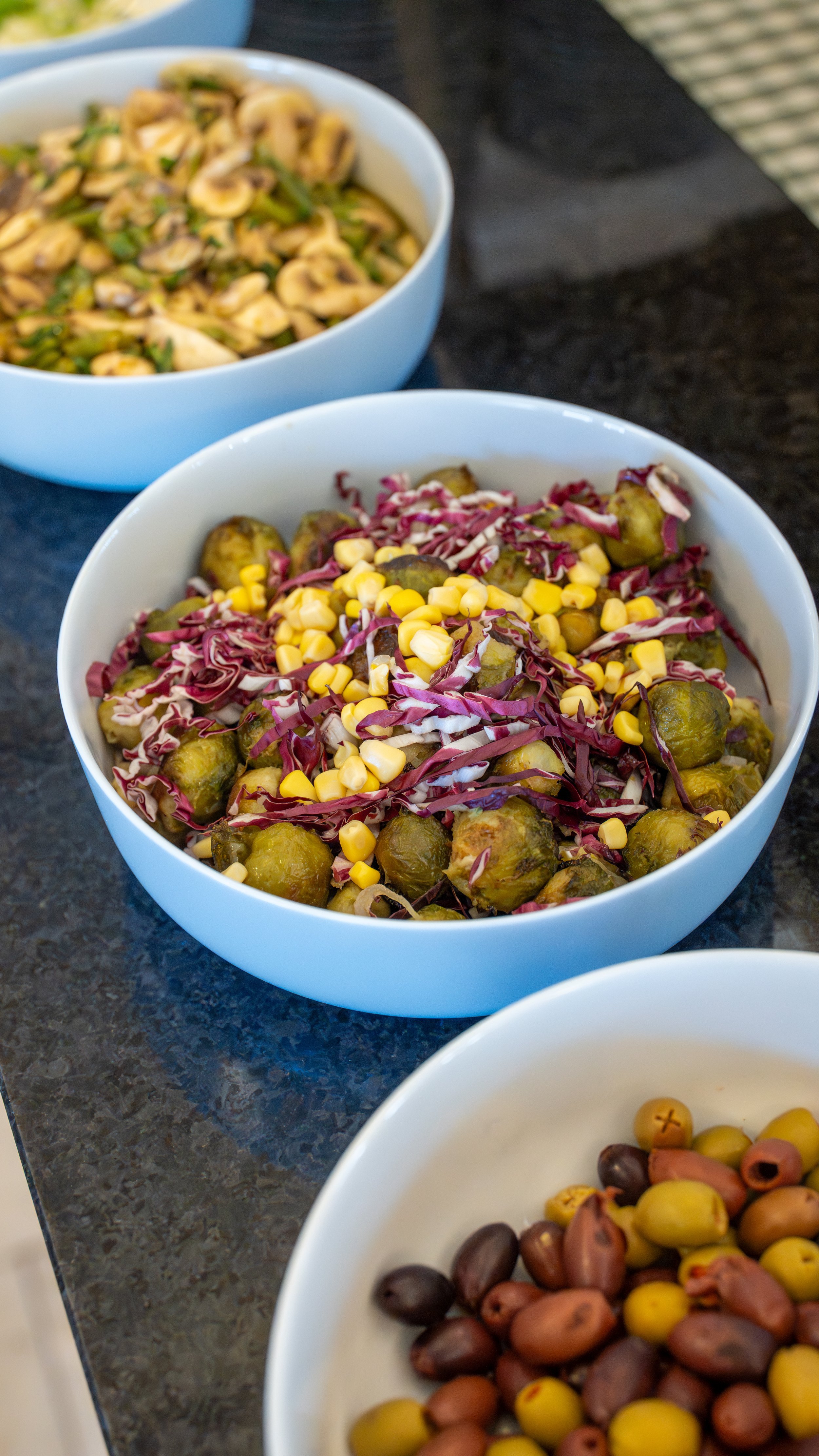 Bowls of mixed salads and snacks on a dark countertop.