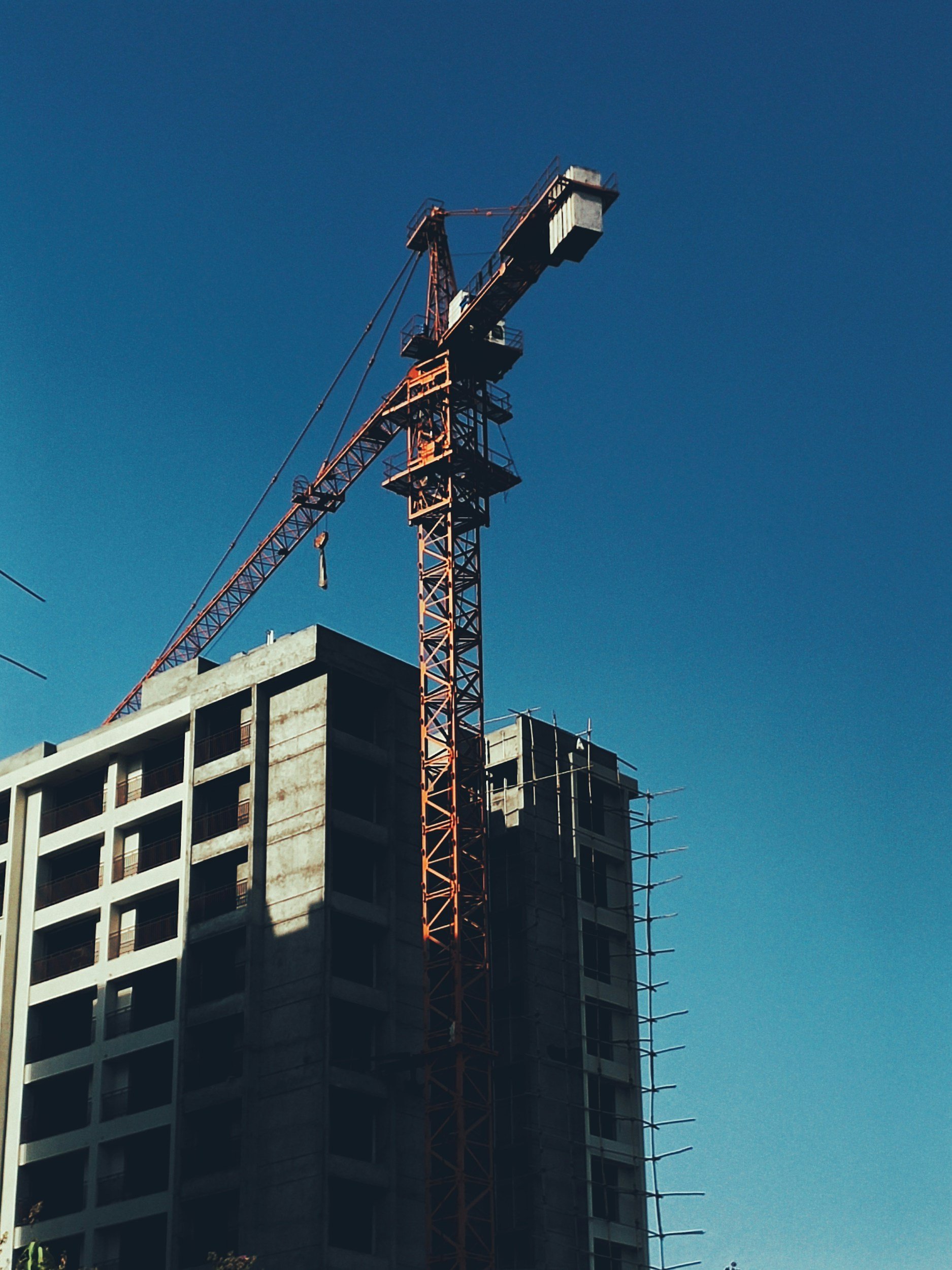 A construction crane is working on a high-rise building under construction against a clear blue sky.