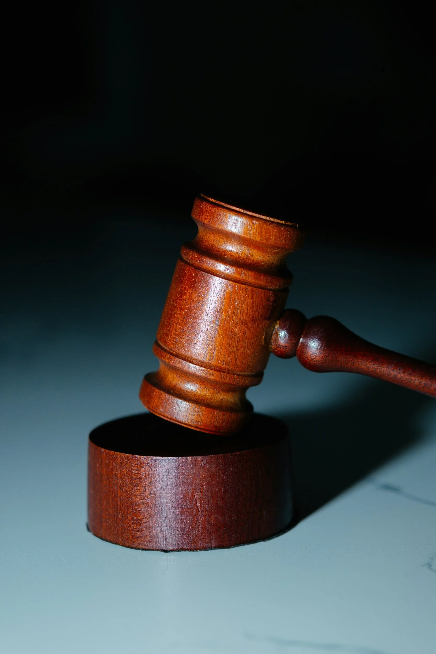 A wooden judge's gavel striking a sound block on a dark surface, with a dark background.