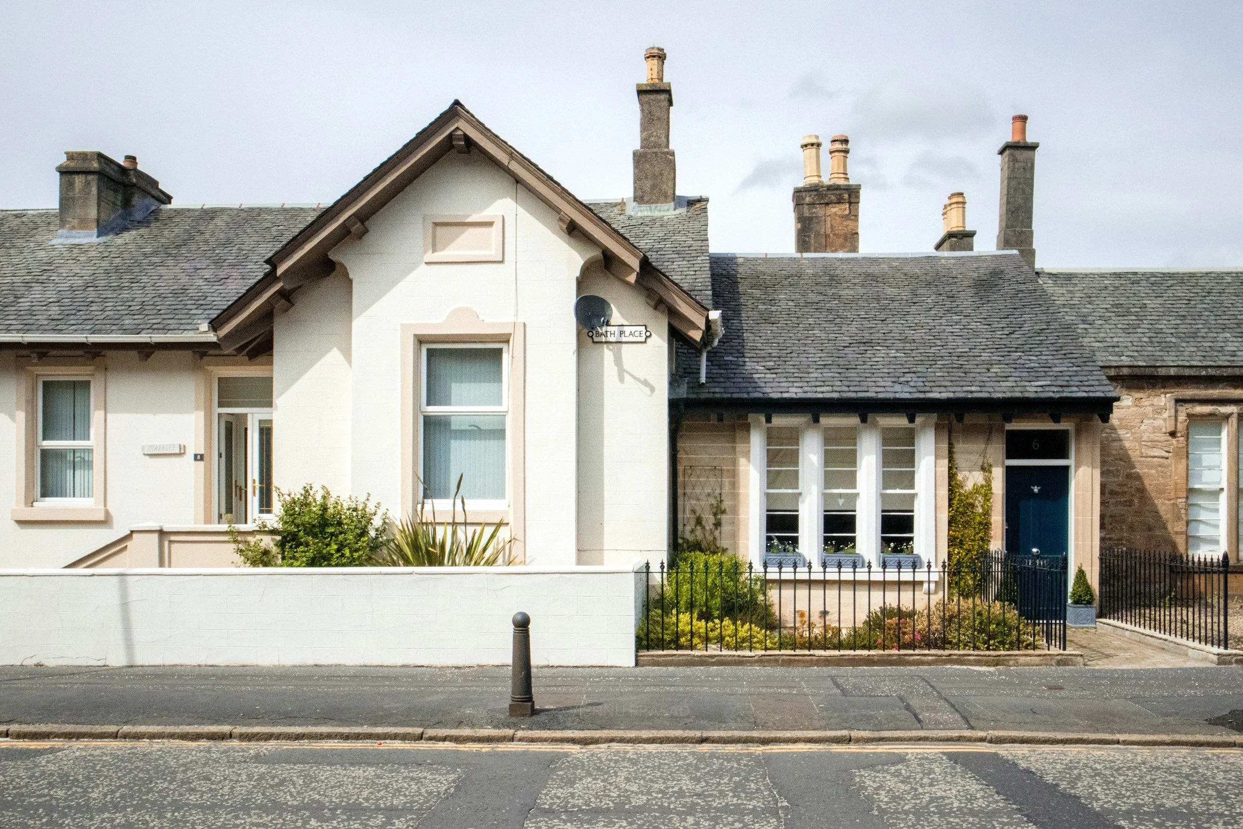 A row of houses on a city street with a white picket fence and a sidewalk in the foreground.