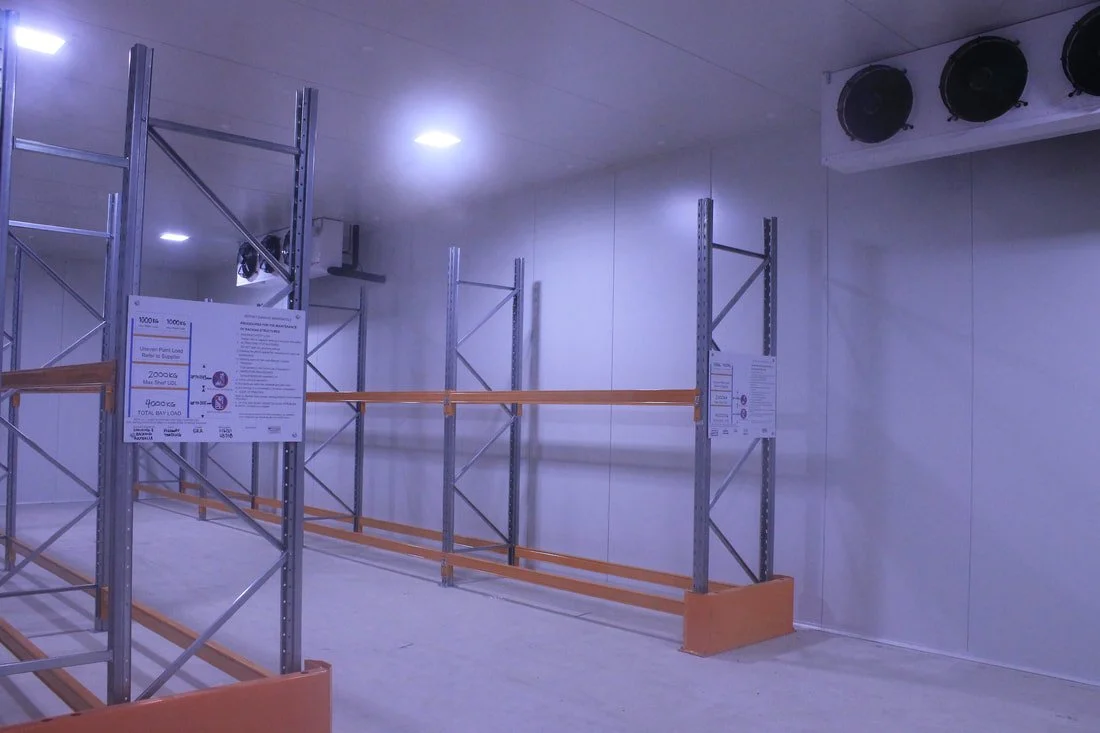 Empty metal and wood retail shelving unit in a store or warehouse, with signs on the shelves and items for sale or storage.