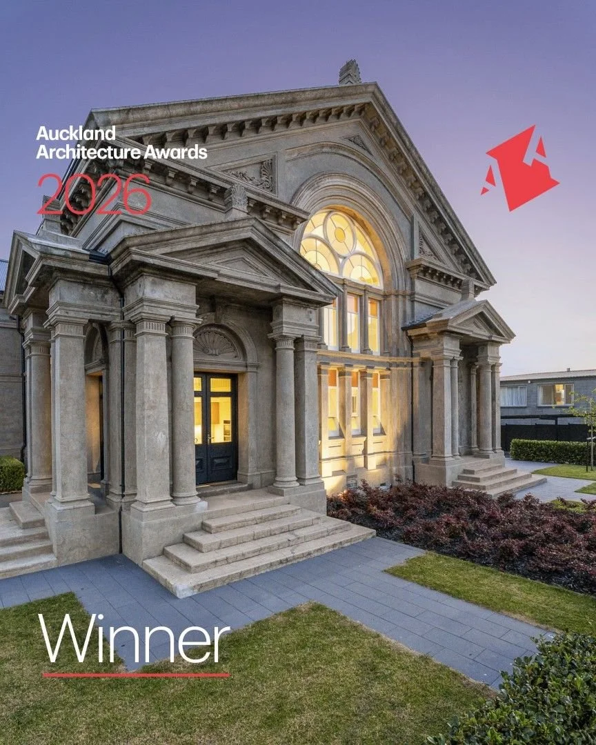 A grand, neoclassical-style heritage building with columns and ornate architectural details, illuminated by exterior lighting during dusk, with a landscaped front yard and pathway.