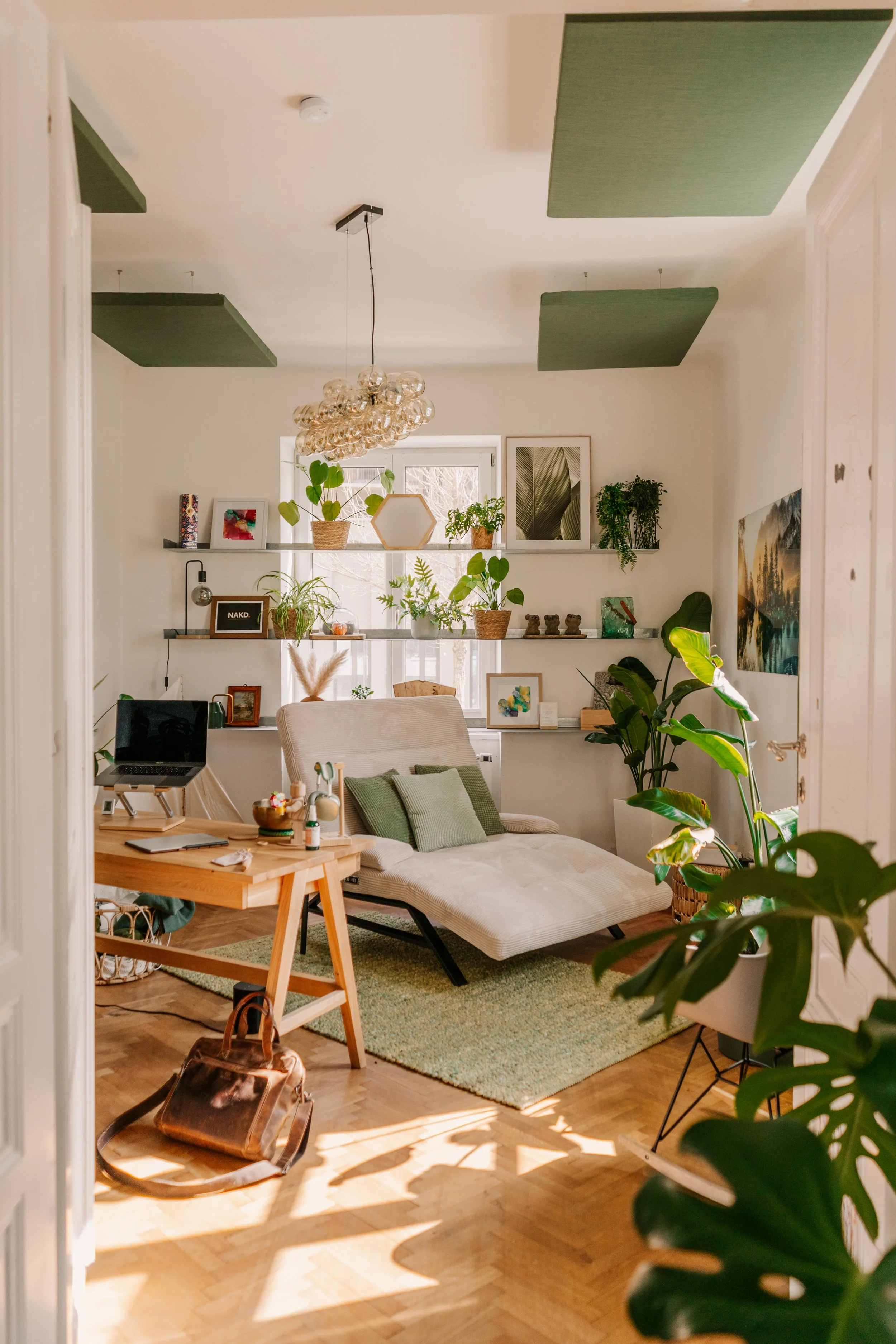 Gemütliches Wohnzimmer mit weißen Wänden, grünen Akustikpaneelen an der Decke, einem beige Couch, einem Holz-Tisch, vielen Pflanzen, einem grünen Teppich und Wanddekorationen.