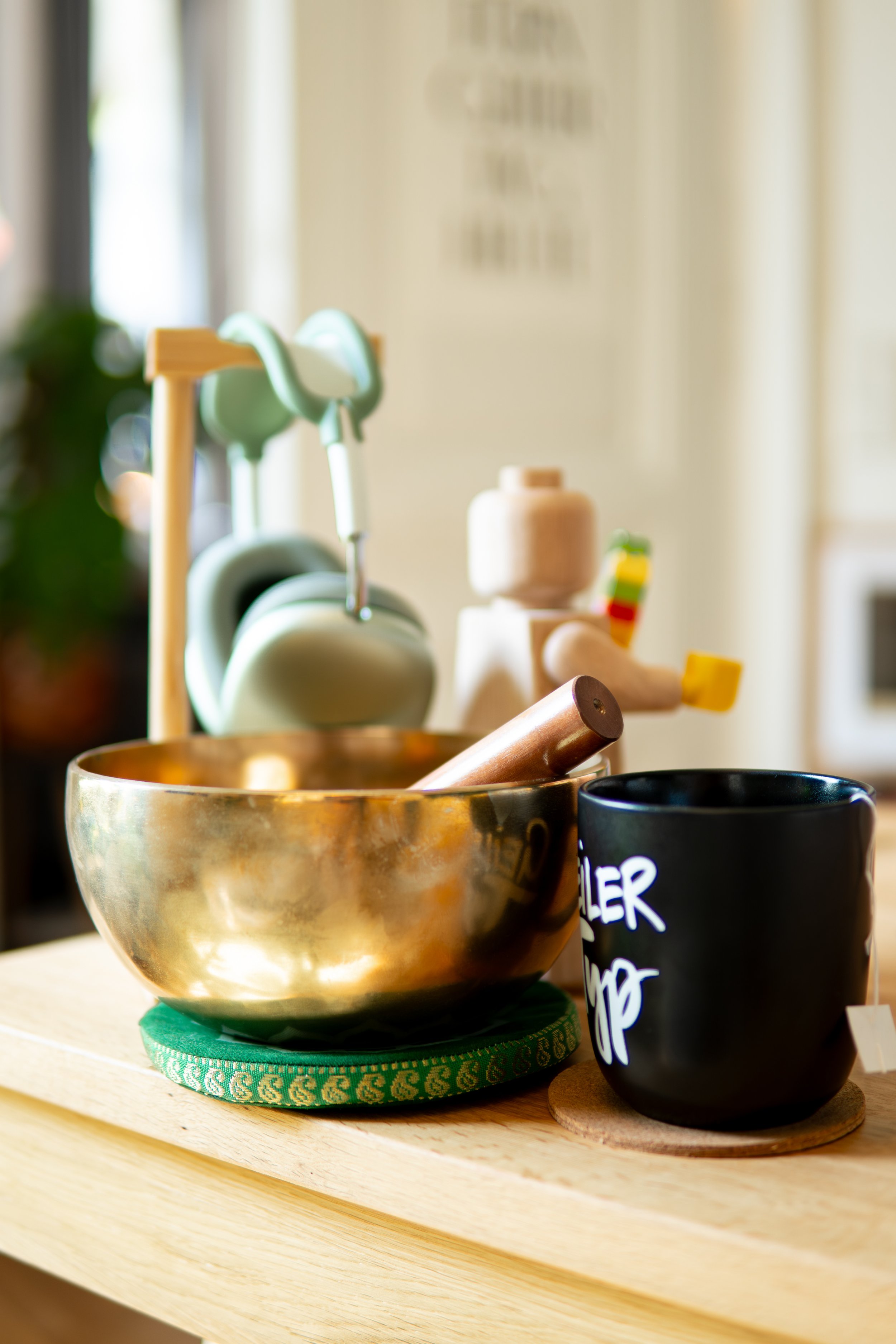 Ein goldener Schüssel mit einem Holzstößel, eine schwarze Tasse mit weißer Schrift, und Küchenutensilien im Hintergrund auf einem Holzbrett