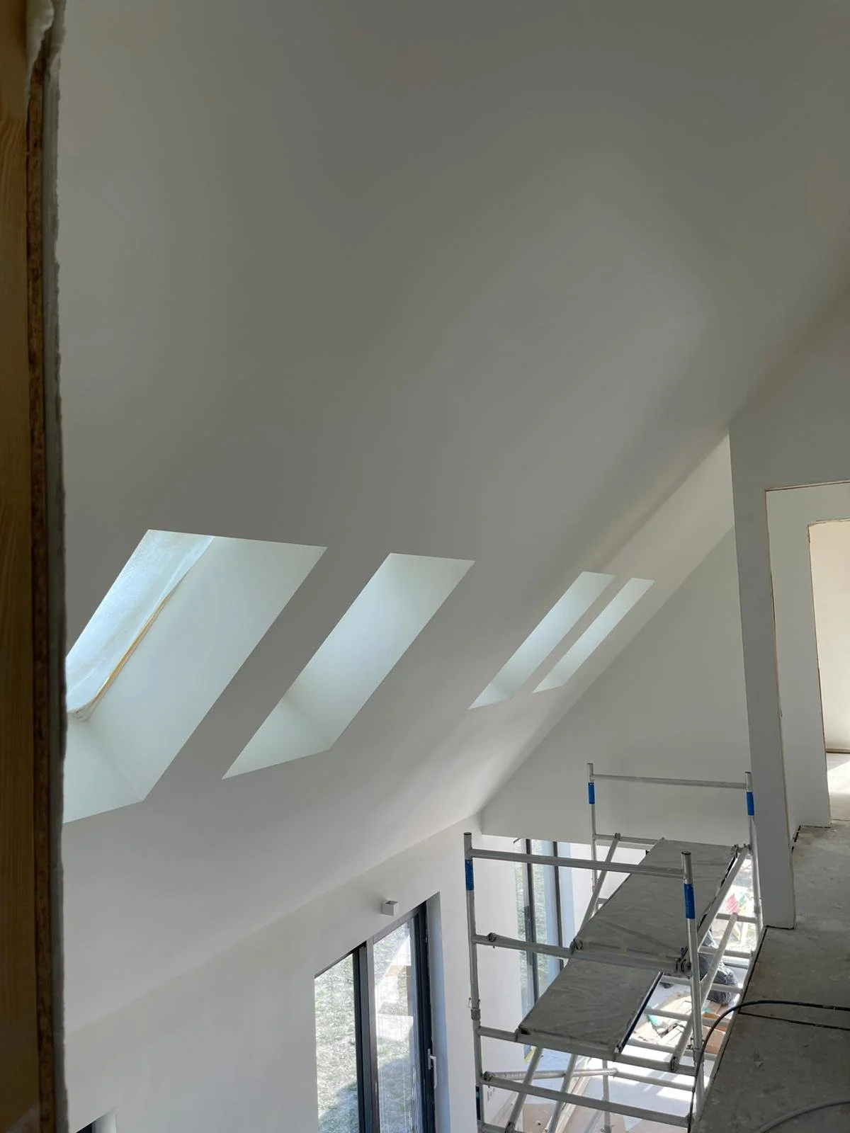 Strakke zolder met schuin dak en dakramen, professioneel gestucte wanden en plafond door stukadoor, nieuwbouw afwerking met glad pleisterwerk en steiger in moderne woning.