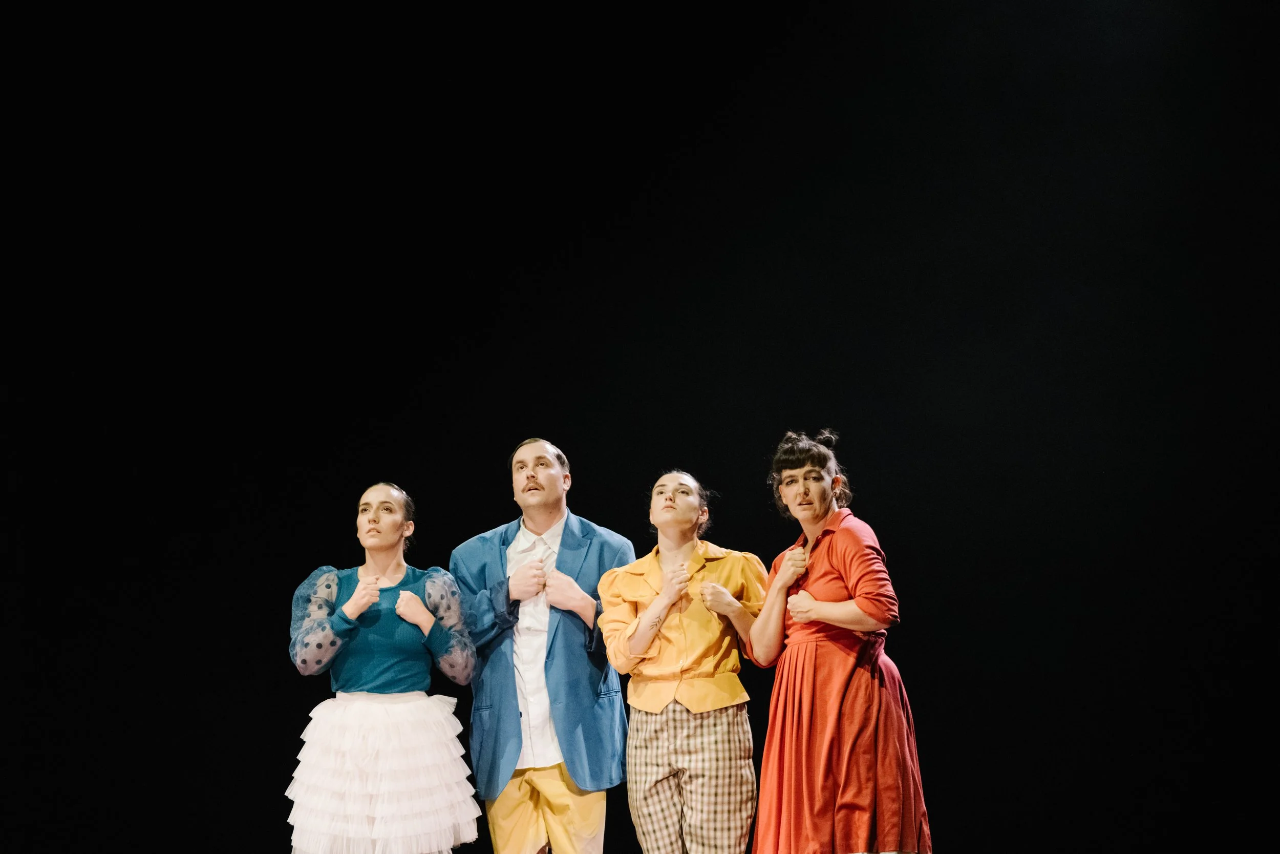 Fünf Schauspielerinnen und Schauspieler stehen auf einer Bühne und schauen nach oben, vor einem schwarzen Hintergrund.