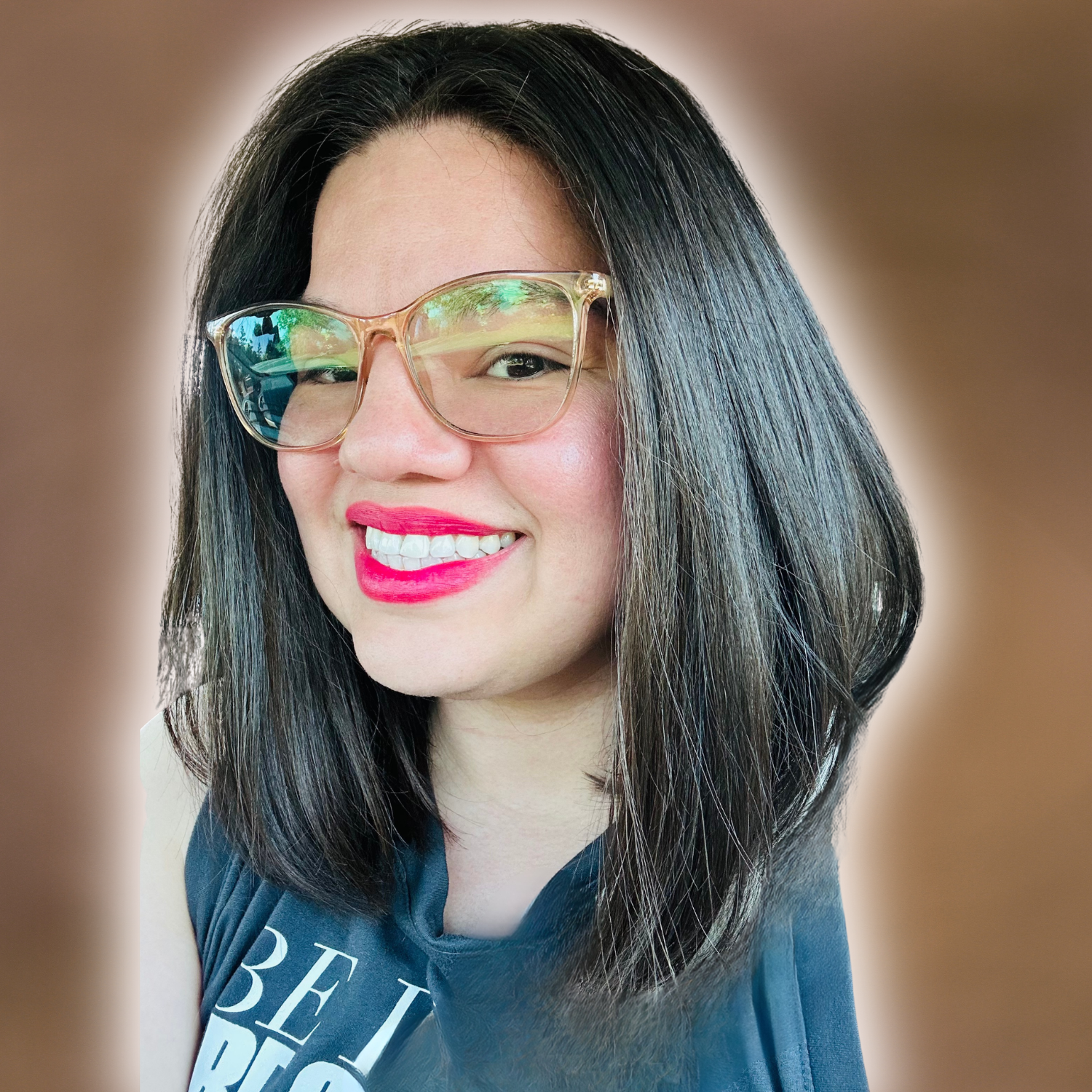 A woman with long dark hair, wearing glasses with a reflection of a window, smiling showing her teeth, with bright pink lipstick, wearing a dark shirt with white letters.