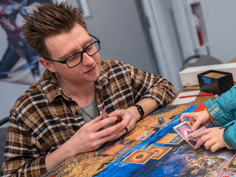 Two people playing a card game at a table, one person is holding cards and the other is looking at cards on the table.