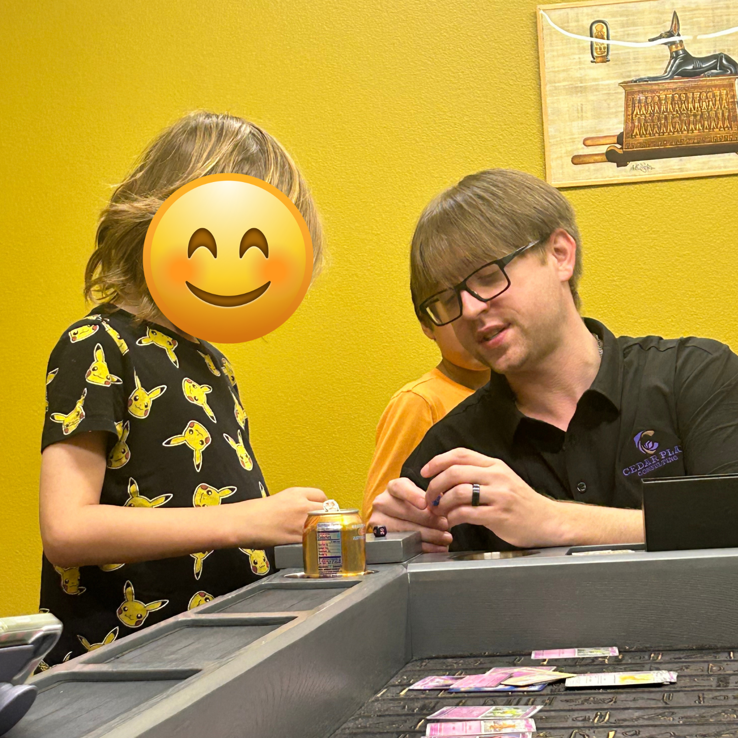 A man and a child playing a Pokémon card game together at a table.