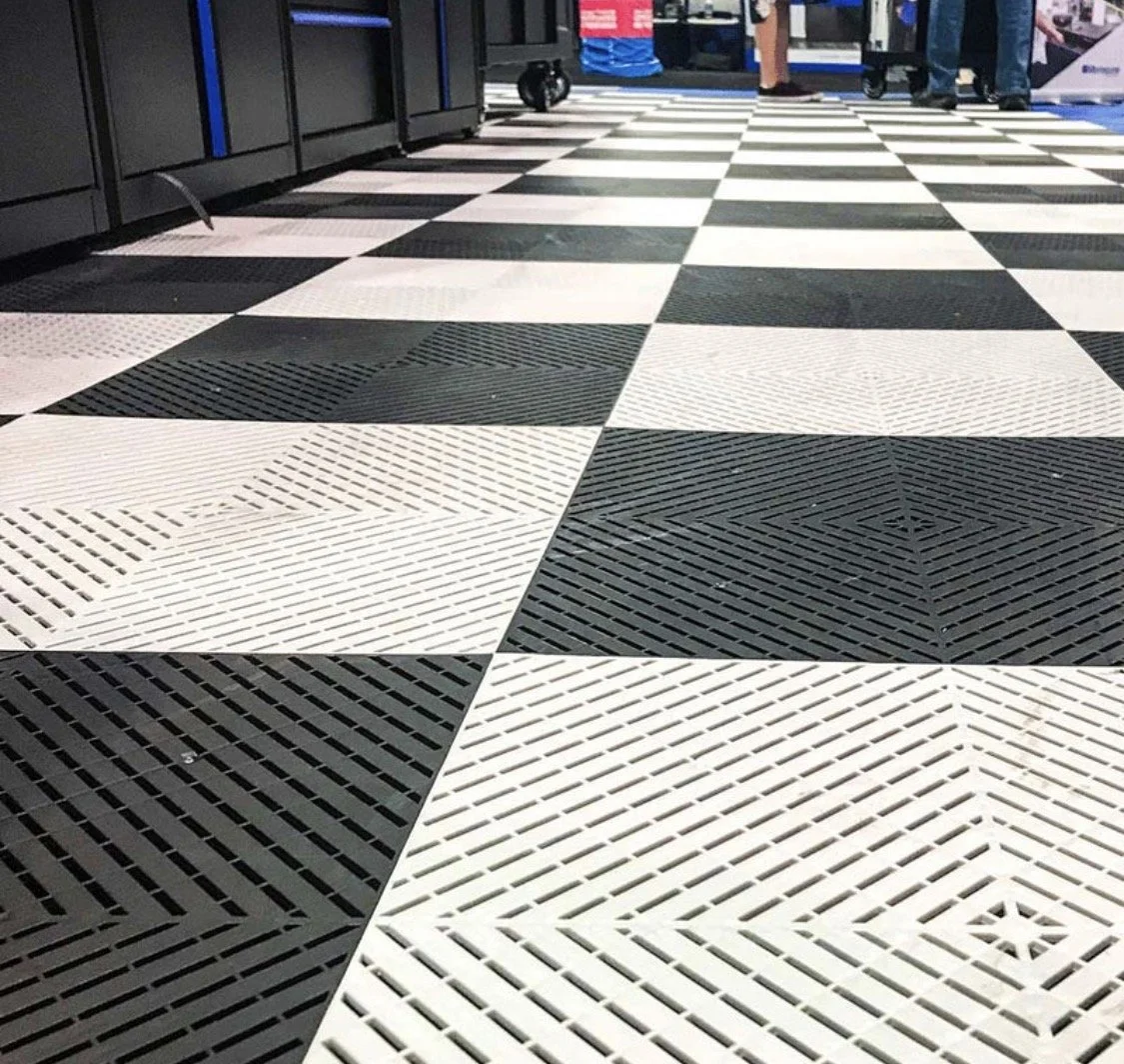 Checkerboard swisstrax floor with black and white tiles in an indoor space, with some people standing in the background.