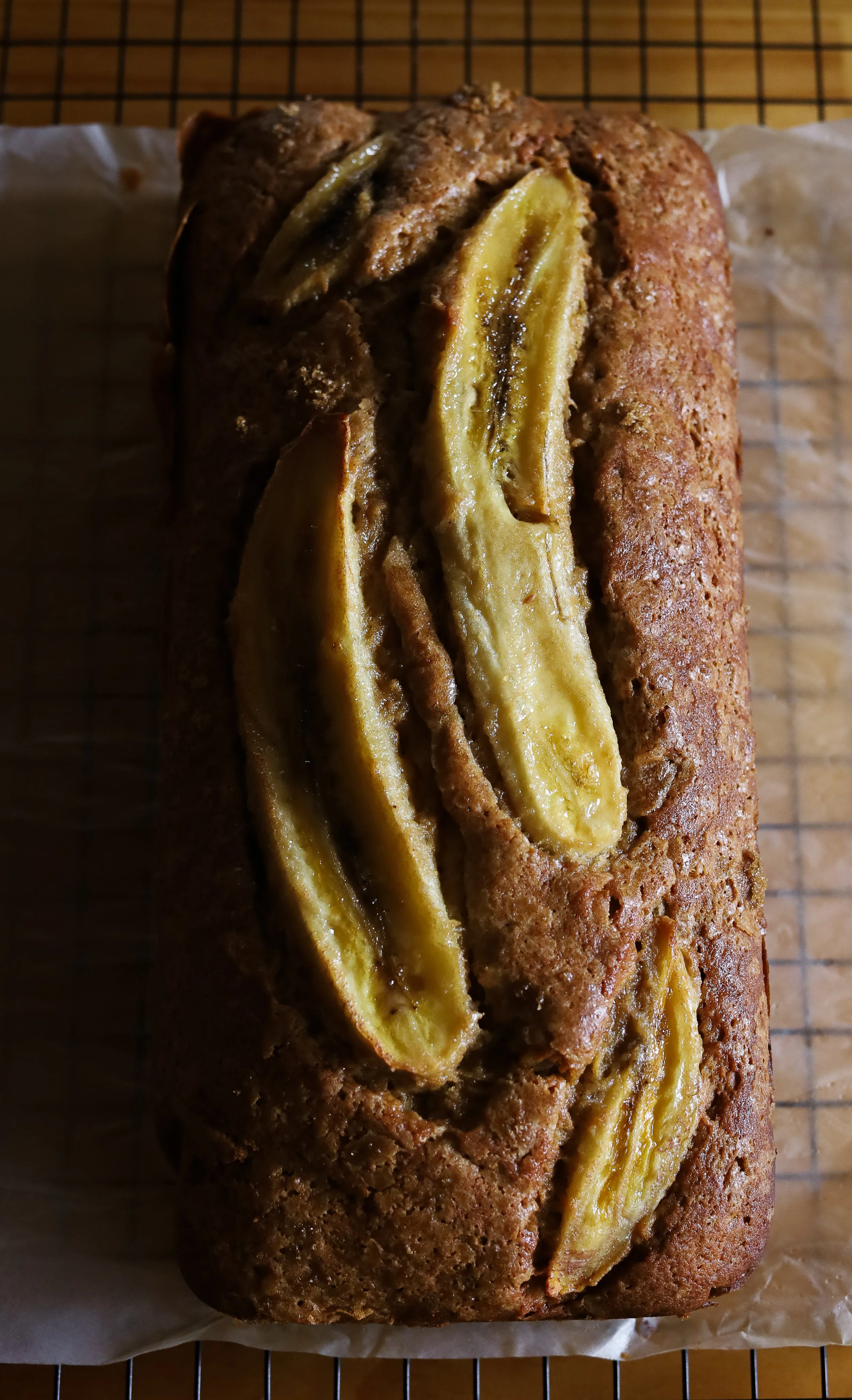 Banana bread with sliced bananas on top, resting on a wire rack.