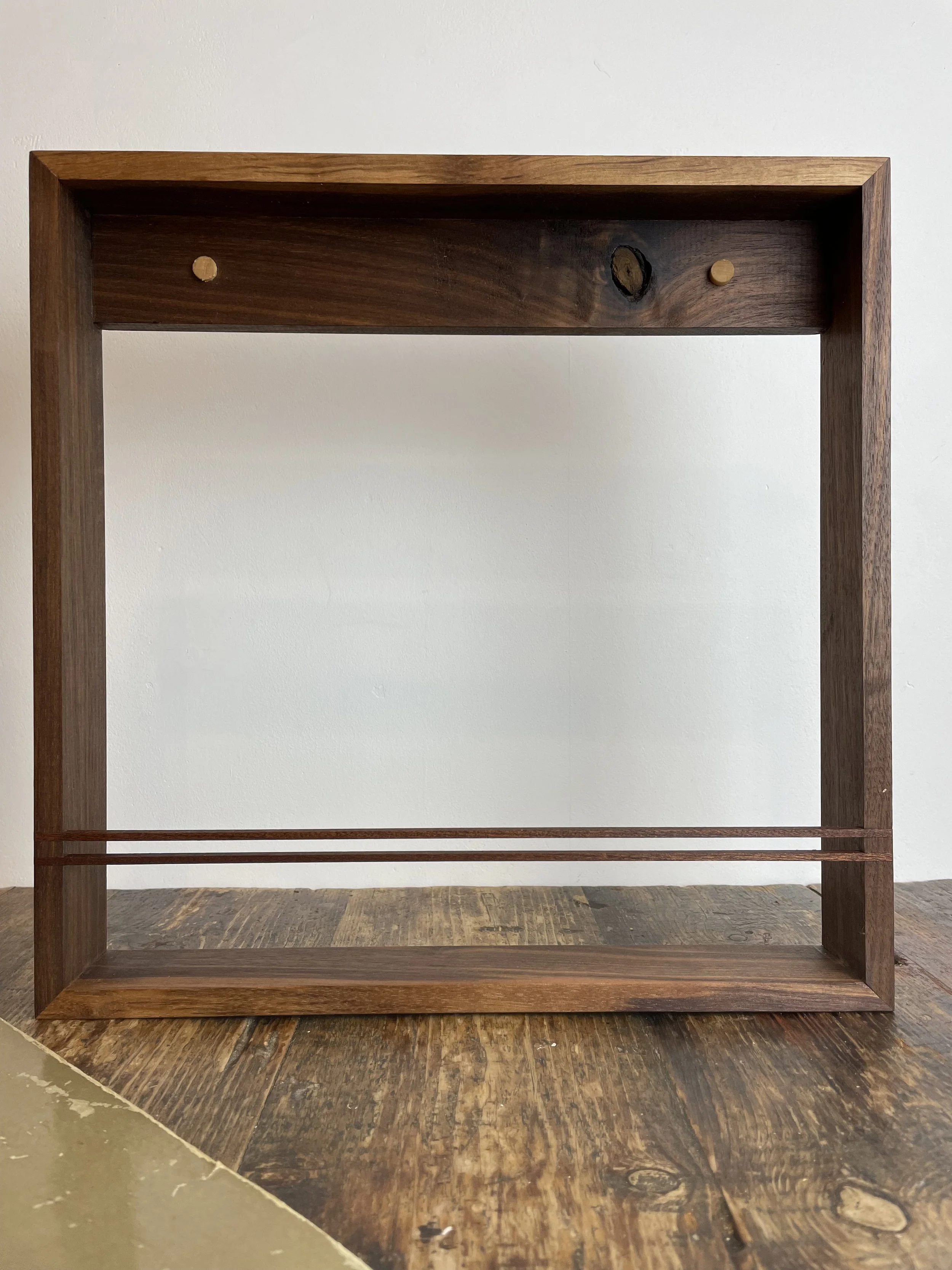 A wooden frame with a rectangular shape, standing on a wooden surface with a white wall in the background.