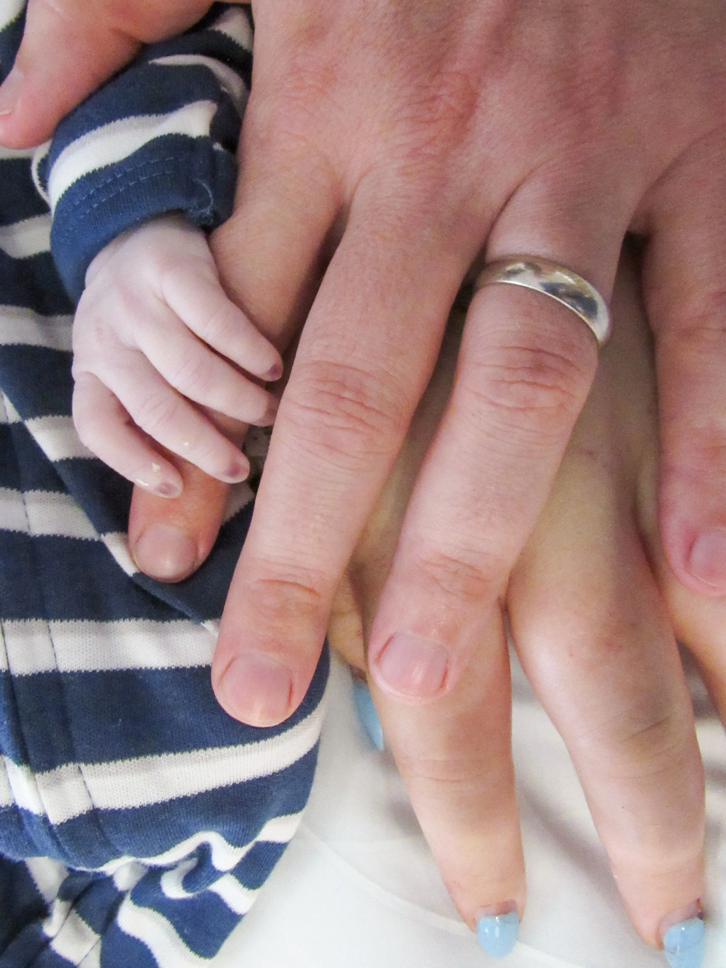 Close-up of a small child's hand gripping an adult's hand, with the adult wearing a silver ring.