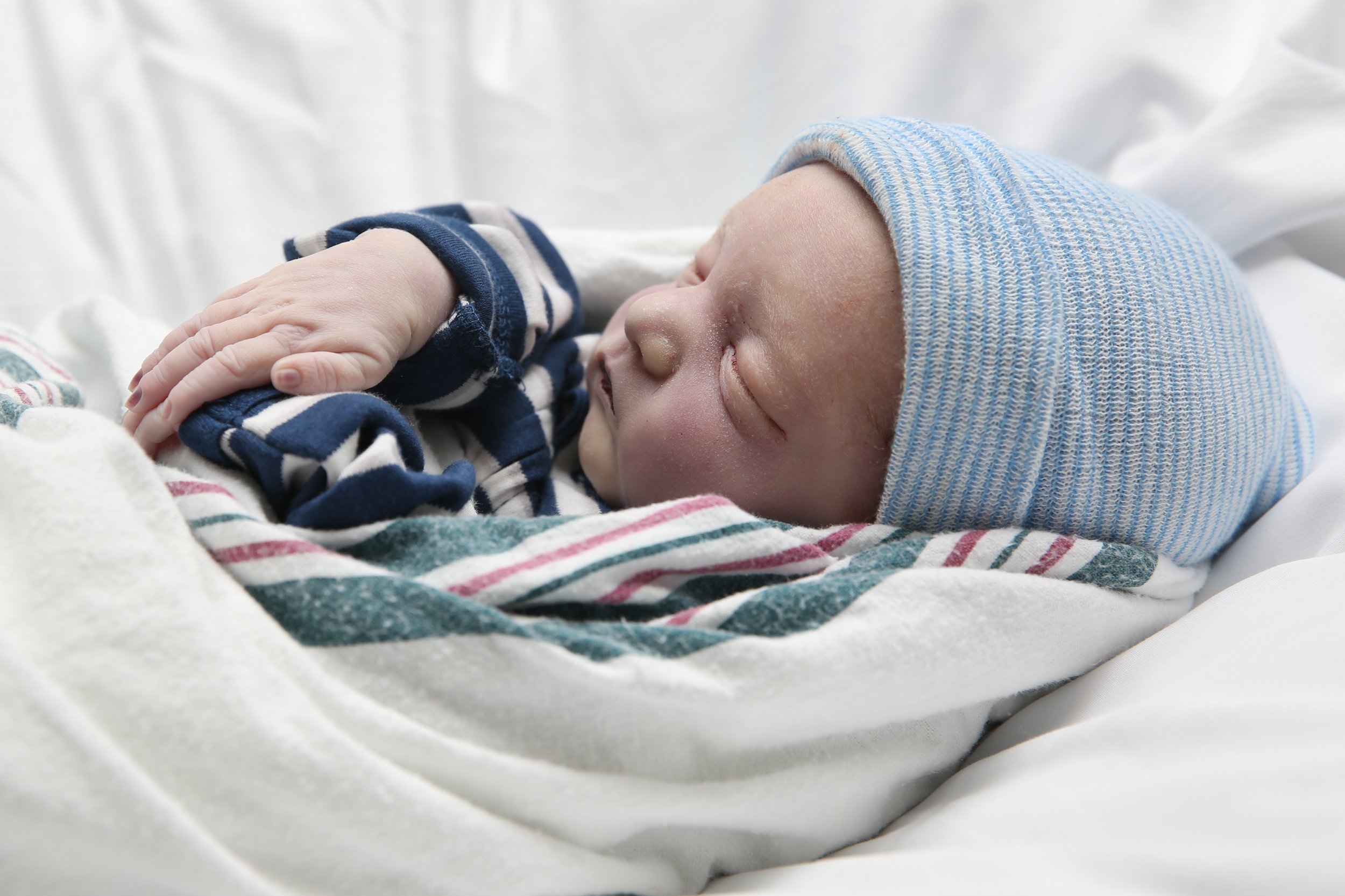 A sleeping newborn baby lying on a hospital bed, wearing a blue striped hat and navy blue and white striped pajamas.