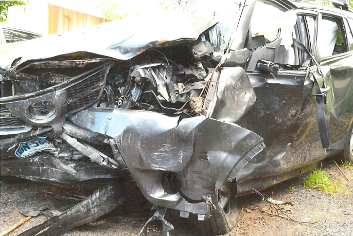 Damaged black car with severe front-end collision, crumpled hood, and missing parts.