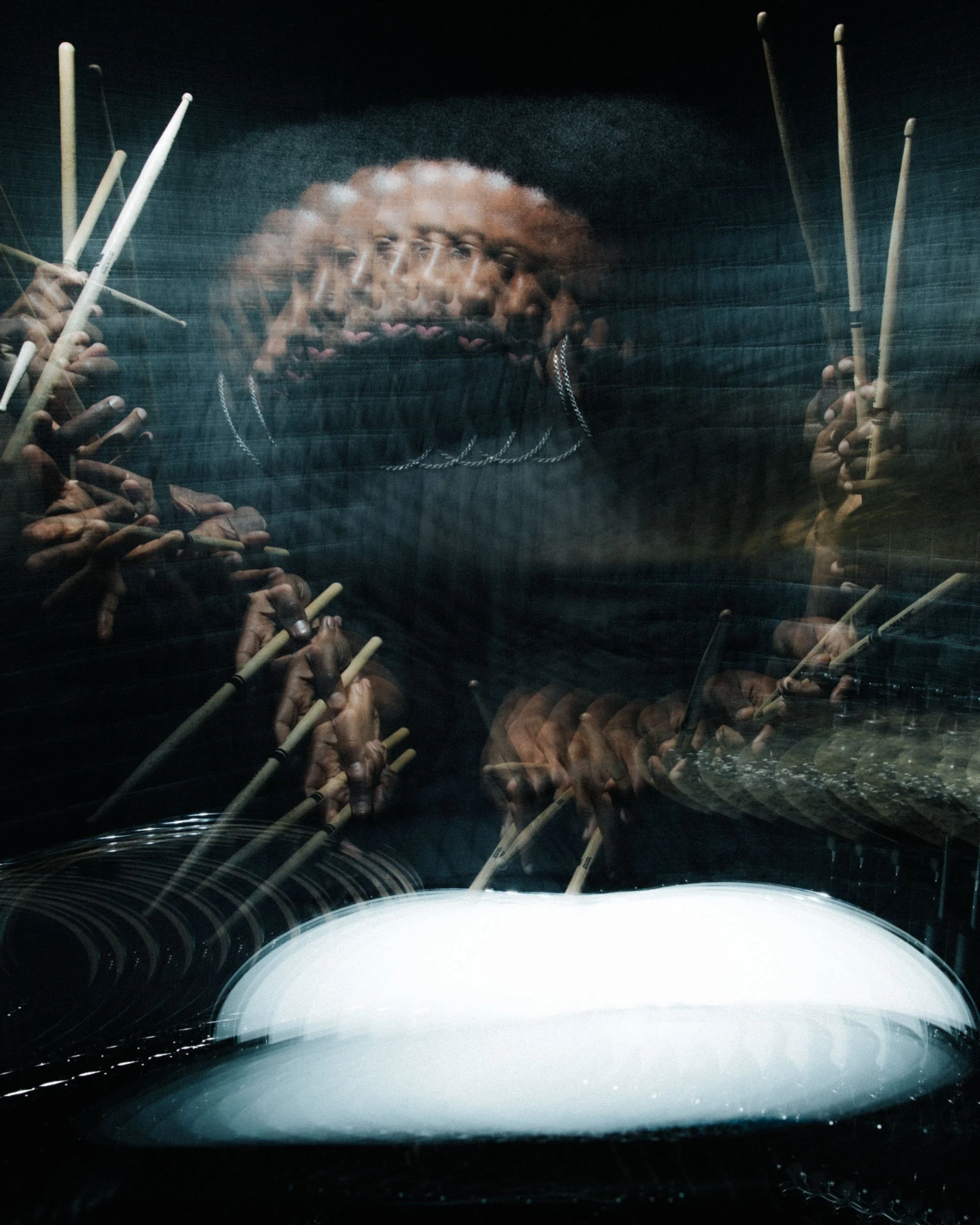 A reflection of multiple overlapping images of a person's face and hands, holding chopsticks, seen through the rear window of a moving vehicle with a white front hood visible at the bottom of the image.