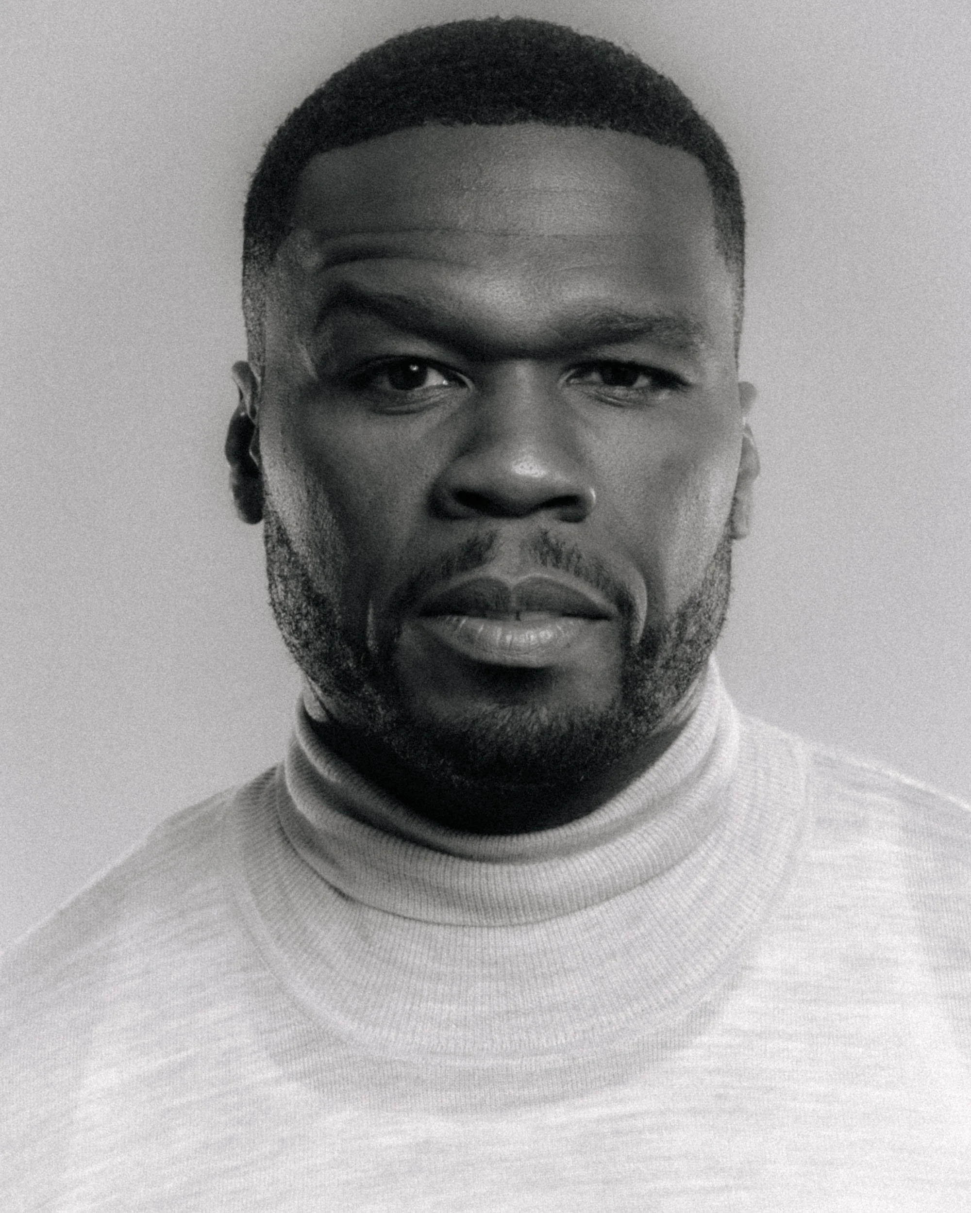 Close-up black and white photo of a young man with short hair, a beard, and wearing a turtleneck sweater.