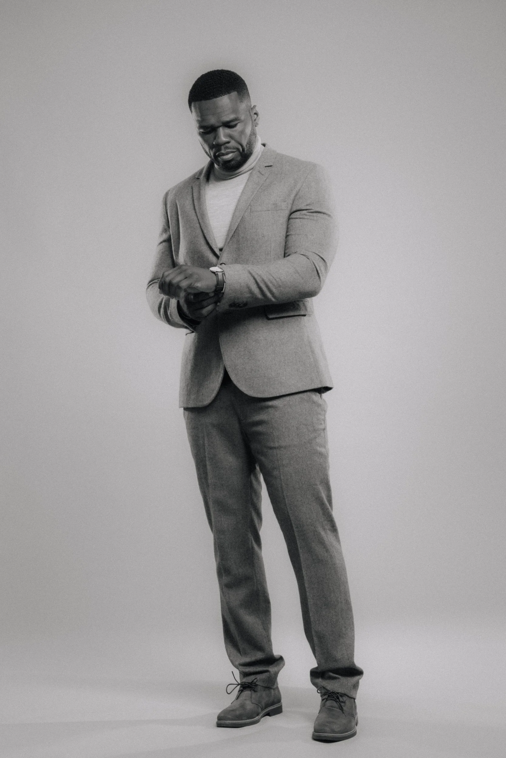 A man wearing a suit checking his watch against a plain background.
