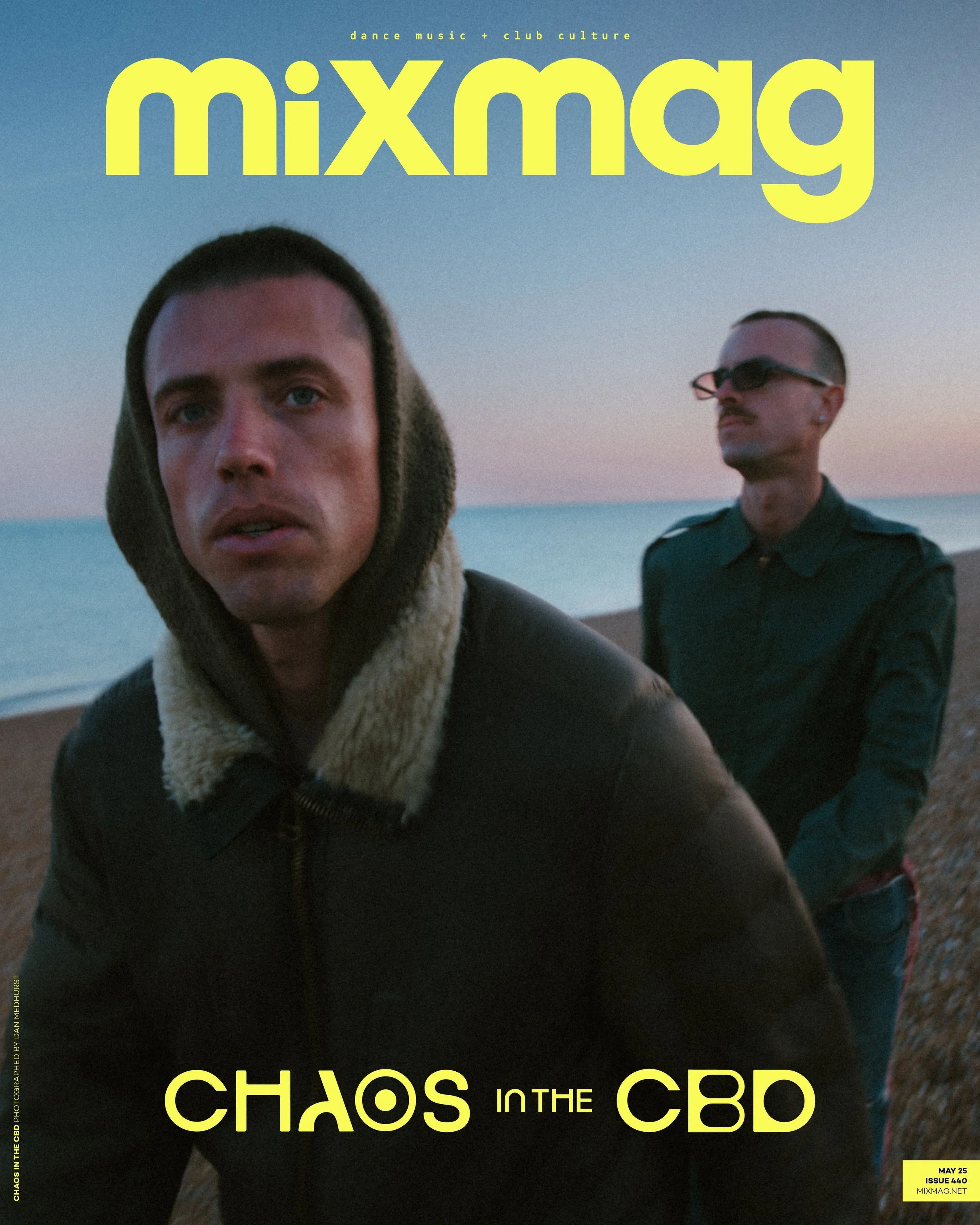 Cover of a magazine titled 'mixmag' with a subtitle 'dance music + club culture'. Features two men with dark hair, one wearing sunglasses, standing outdoors during sunset or sunrise by the water. The main headline reads 'CHAOS IN THE CBD'.