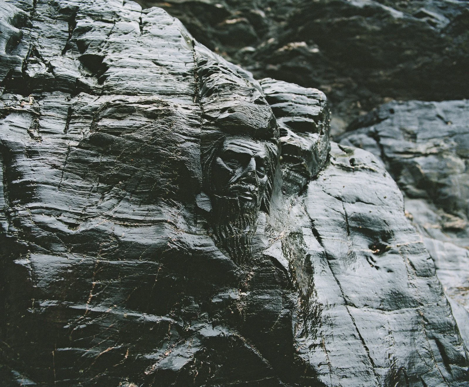 Close-up of a black, shiny, textured rock surface with carved face details.
