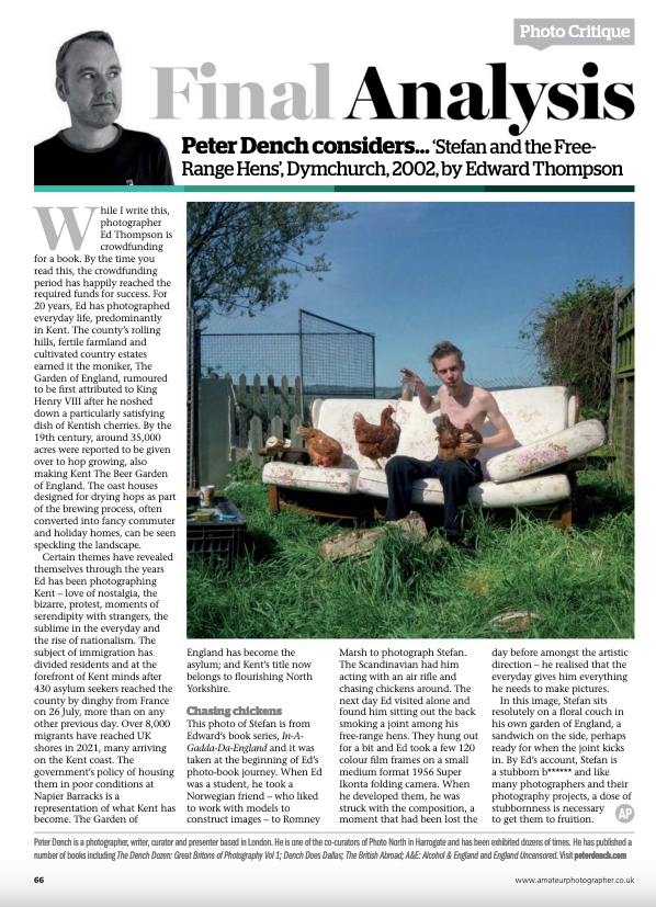 Photograph of a young man sitting on a couch outdoors in a garden, holding a chicken, with two other chickens on the couch. There is a badminton net in the background and a clear blue sky.