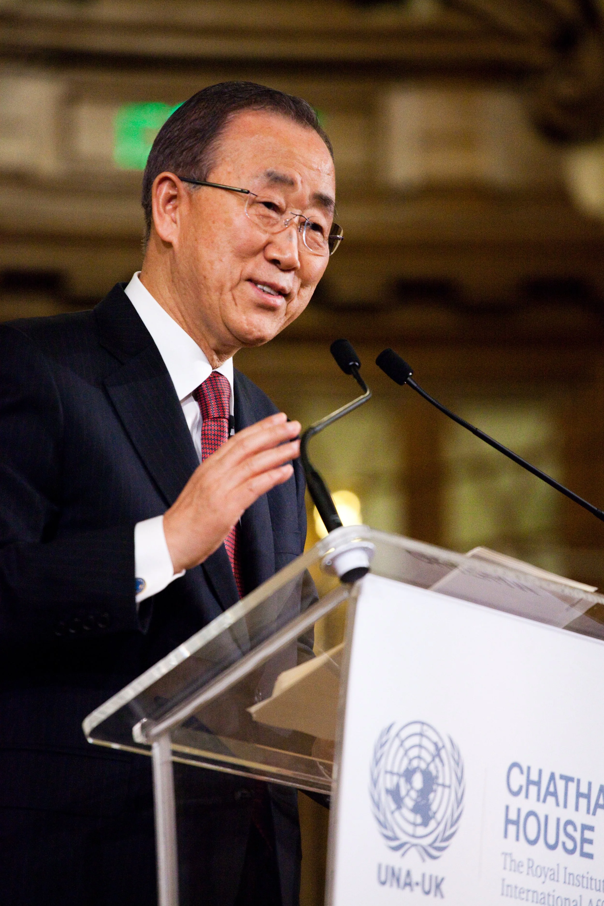 A man in a suit and glasses speaking at a podium with a United Nations logo and a sign that says "Chatham House."