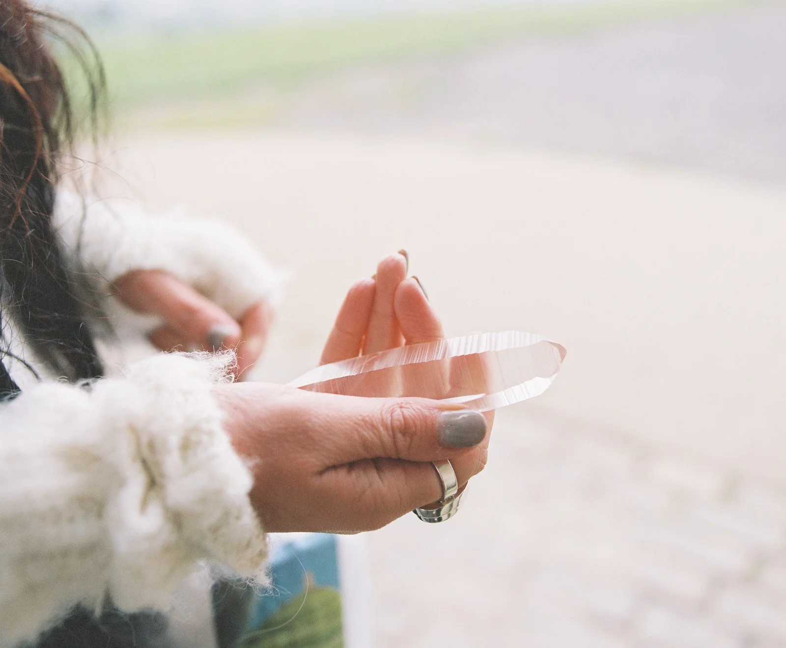 Person holding a large, polished, transparent pink crystal with a natural, textured edge, outdoors in front of a blurred background.