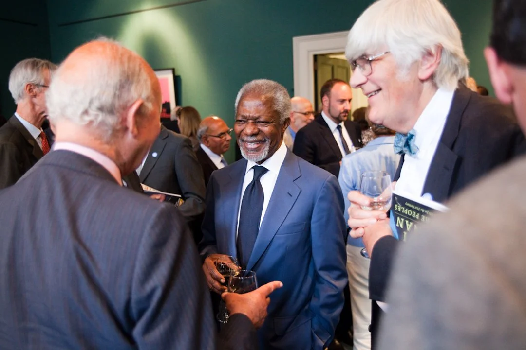Group of men in suits at a social event, smiling and holding glasses of wine.