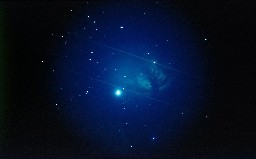 A clear night sky with numerous stars and a bright celestial object amidst a faint nebula.