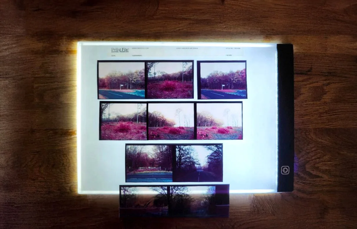 A sheet of printed photographs illuminated by a light box on a wooden surface.