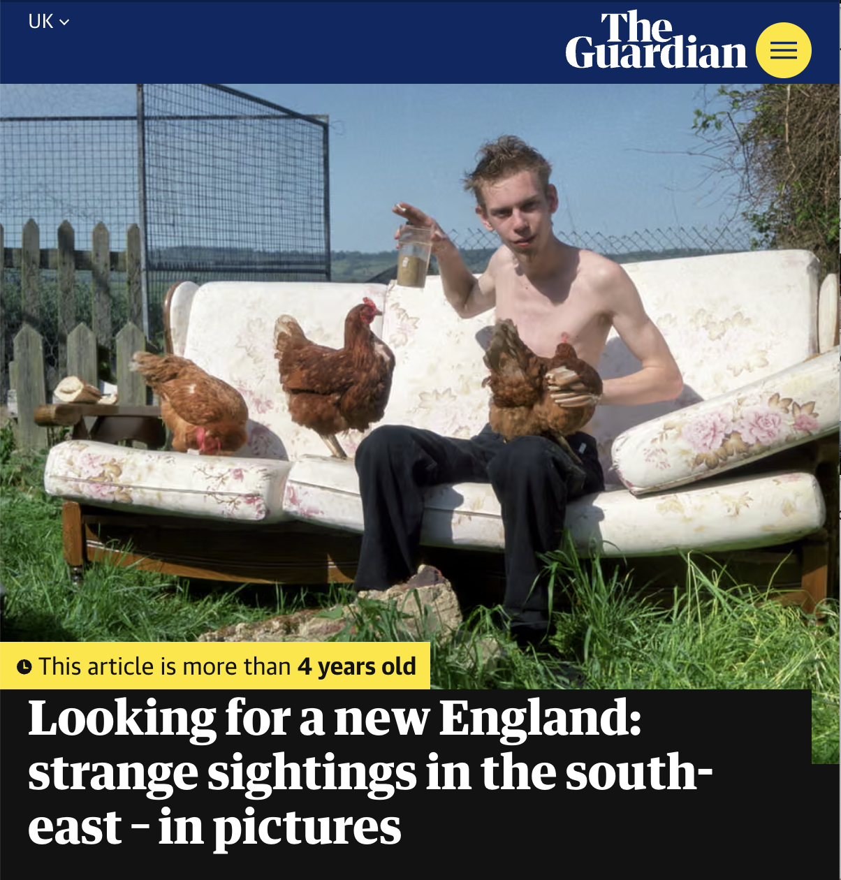 A shirtless young man with messy hair sitting on a floral-patterned sofa outdoors, holding chickens, with two more chickens on the sofa. The scene is set in a rural backyard with grass, a wooden fence, and a blue sky.