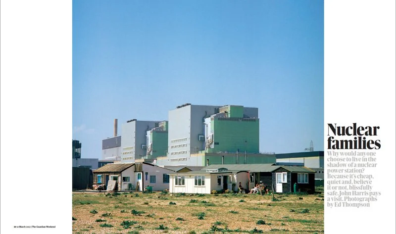 Image of a nuclear power plant with some small houses in the foreground and a clear blue sky.