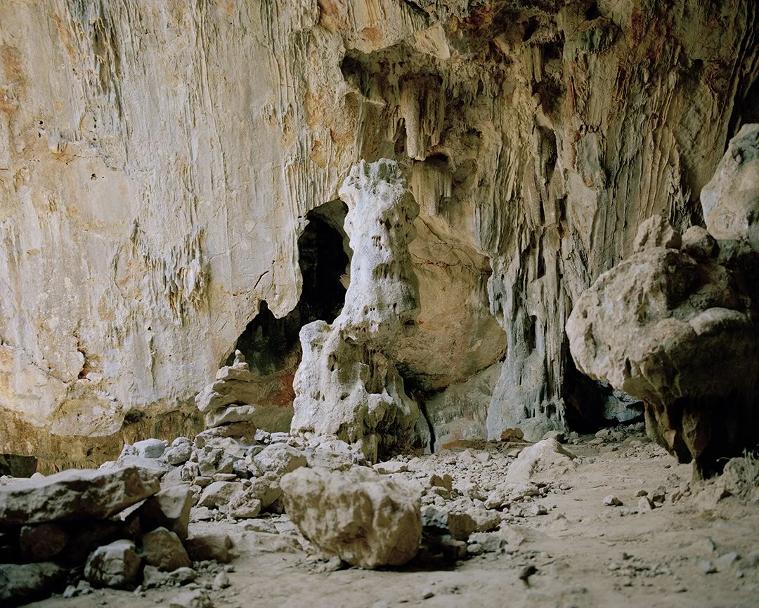 Inside a limestone cave with rocks and stalactites on the walls and a large stalagmite on the ground.
