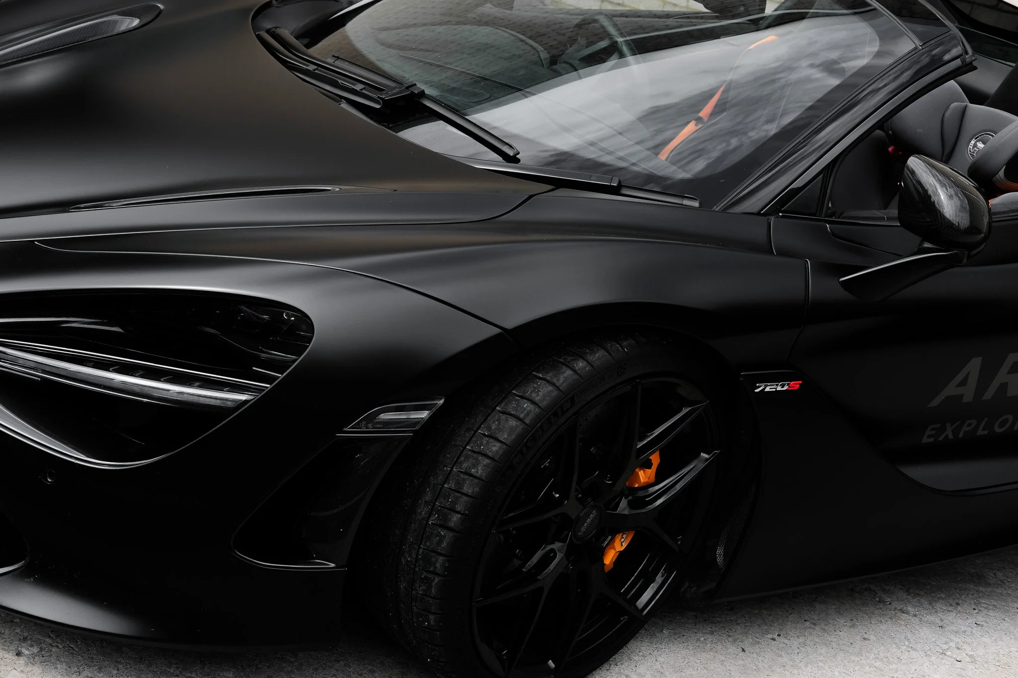 Close-up of a black sports car, showcasing the driver's side, including the front wheel, side mirror, and part of the windshield.