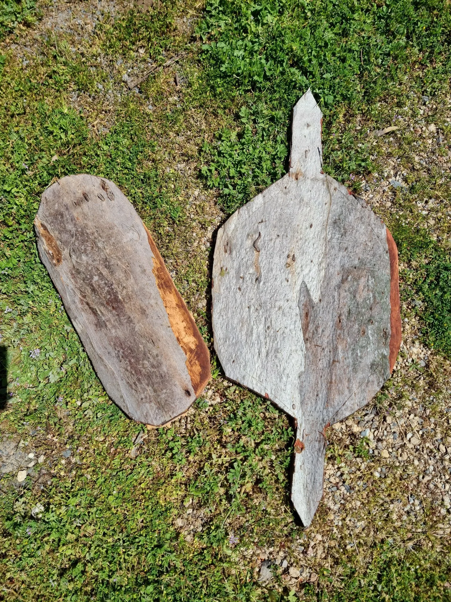 A wooden coolamon and shield on the ground next to eachother.