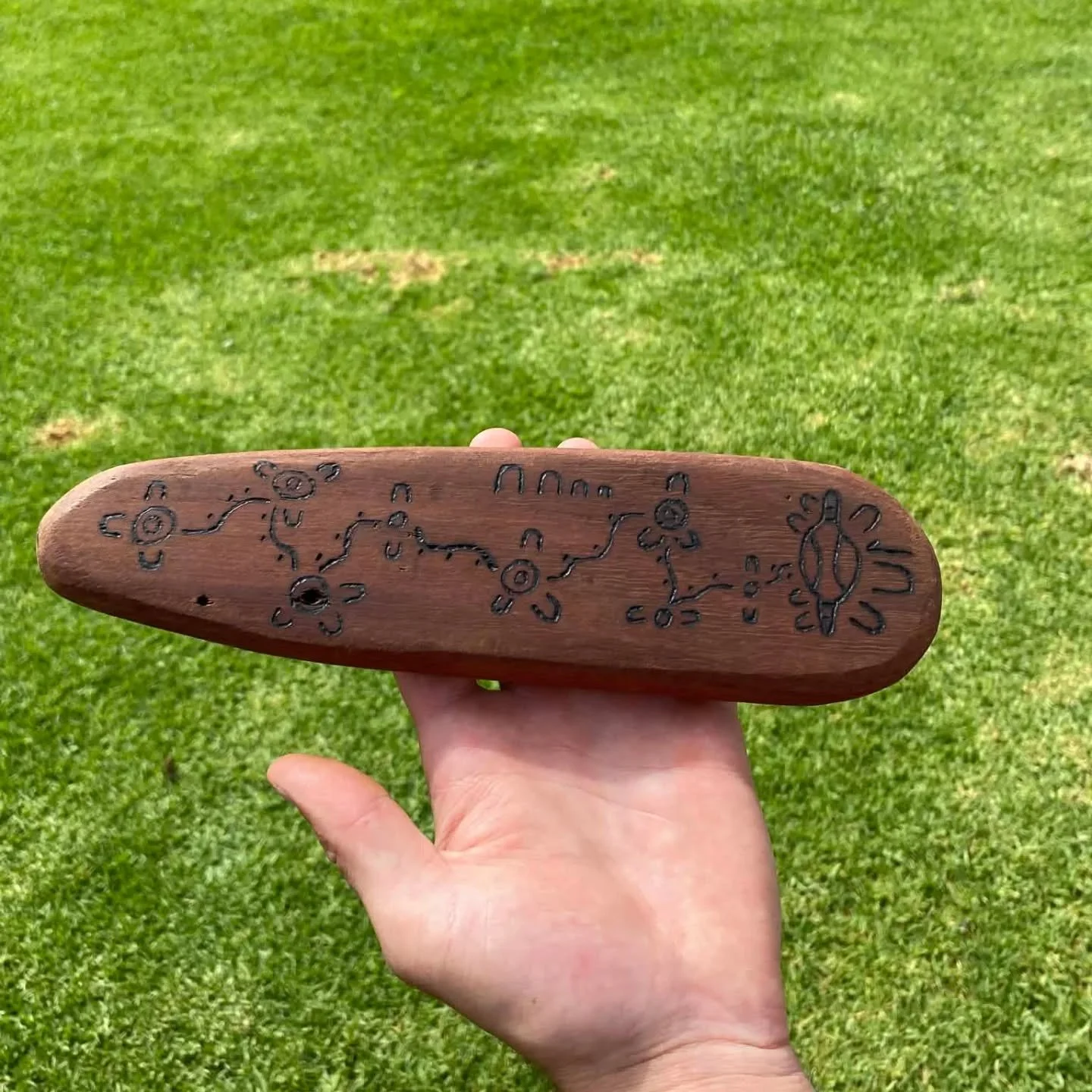 A hand holding an engraved wooden message stick.