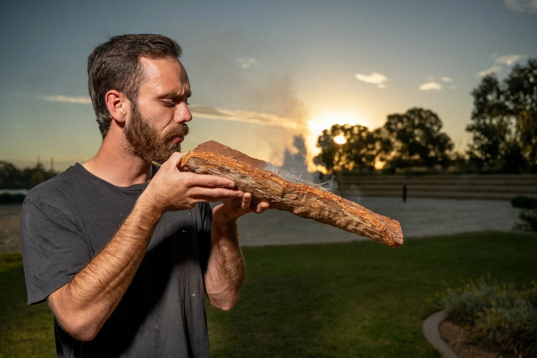 Young Aboriginal man holding a coolamon and blowing smoke during smoking ceremony.