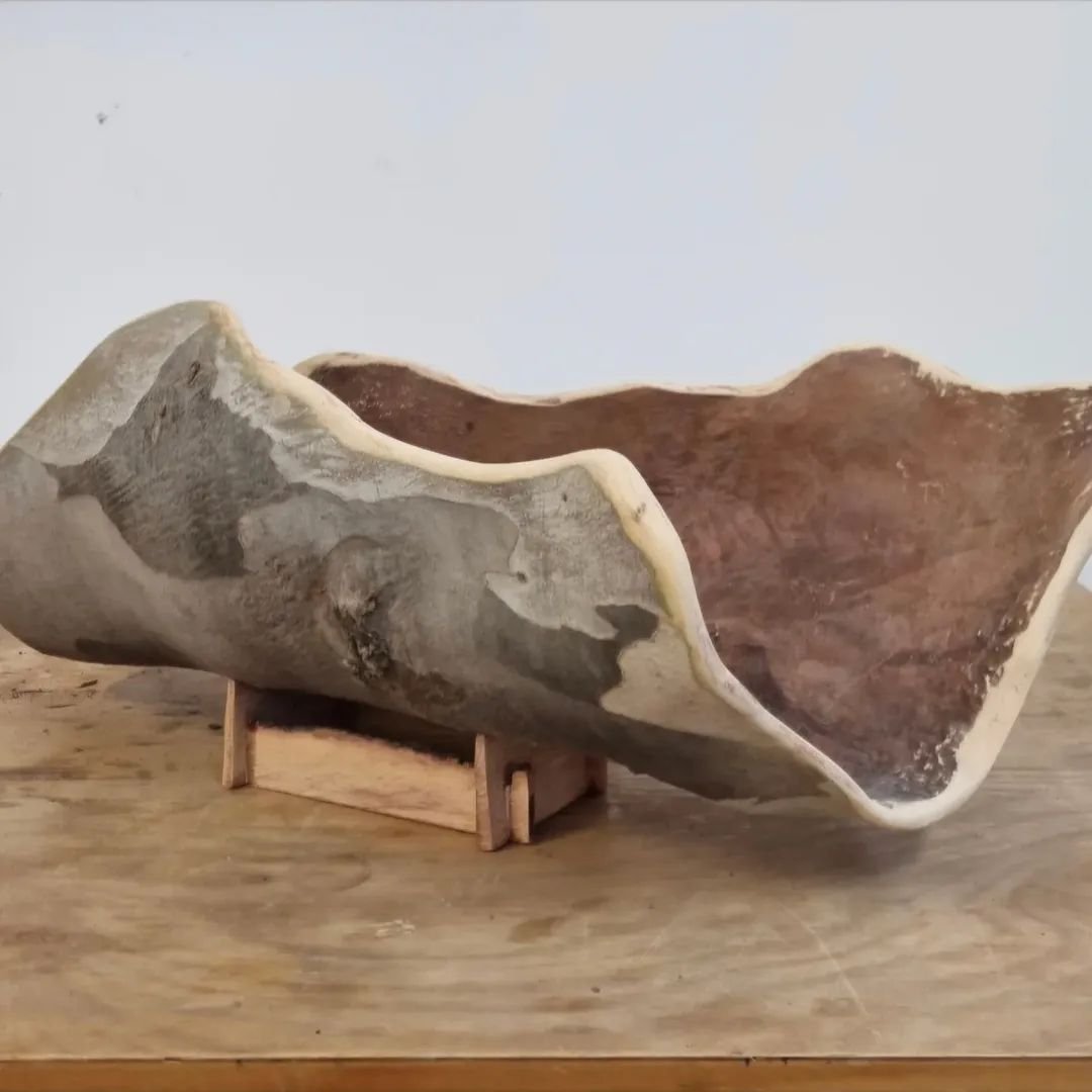A curved coolamon on a wooden stand.