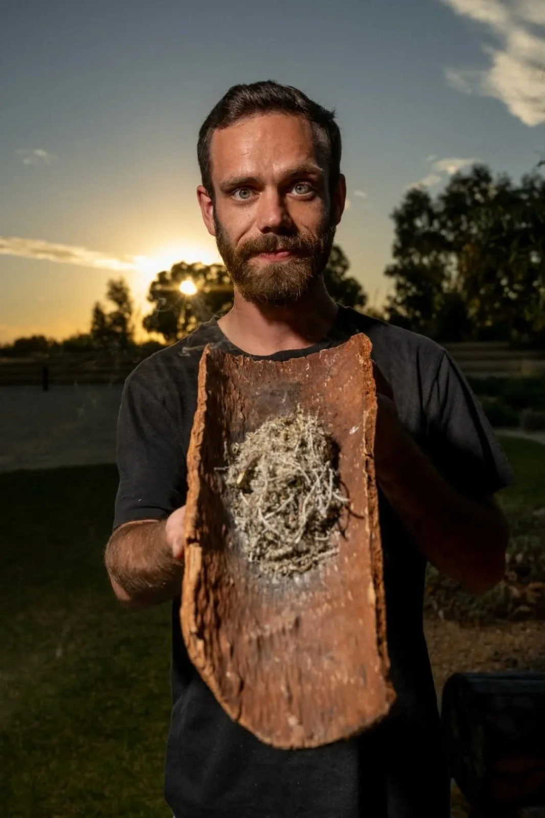 Young Aboriginal man holding a coolamon with dried native plant material at sunset.