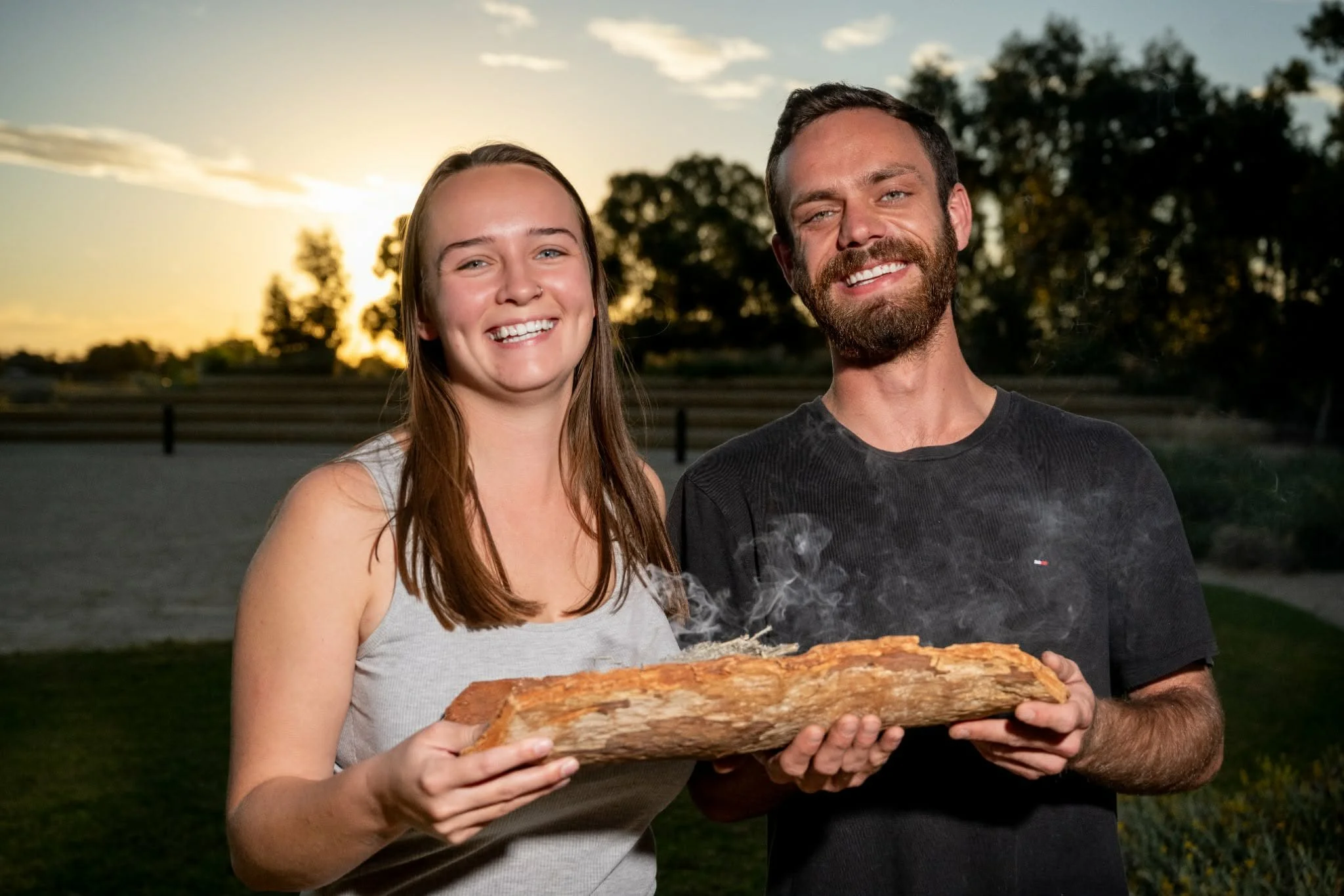 Young Aboriginal woman and man holding a coolamon at sunset.