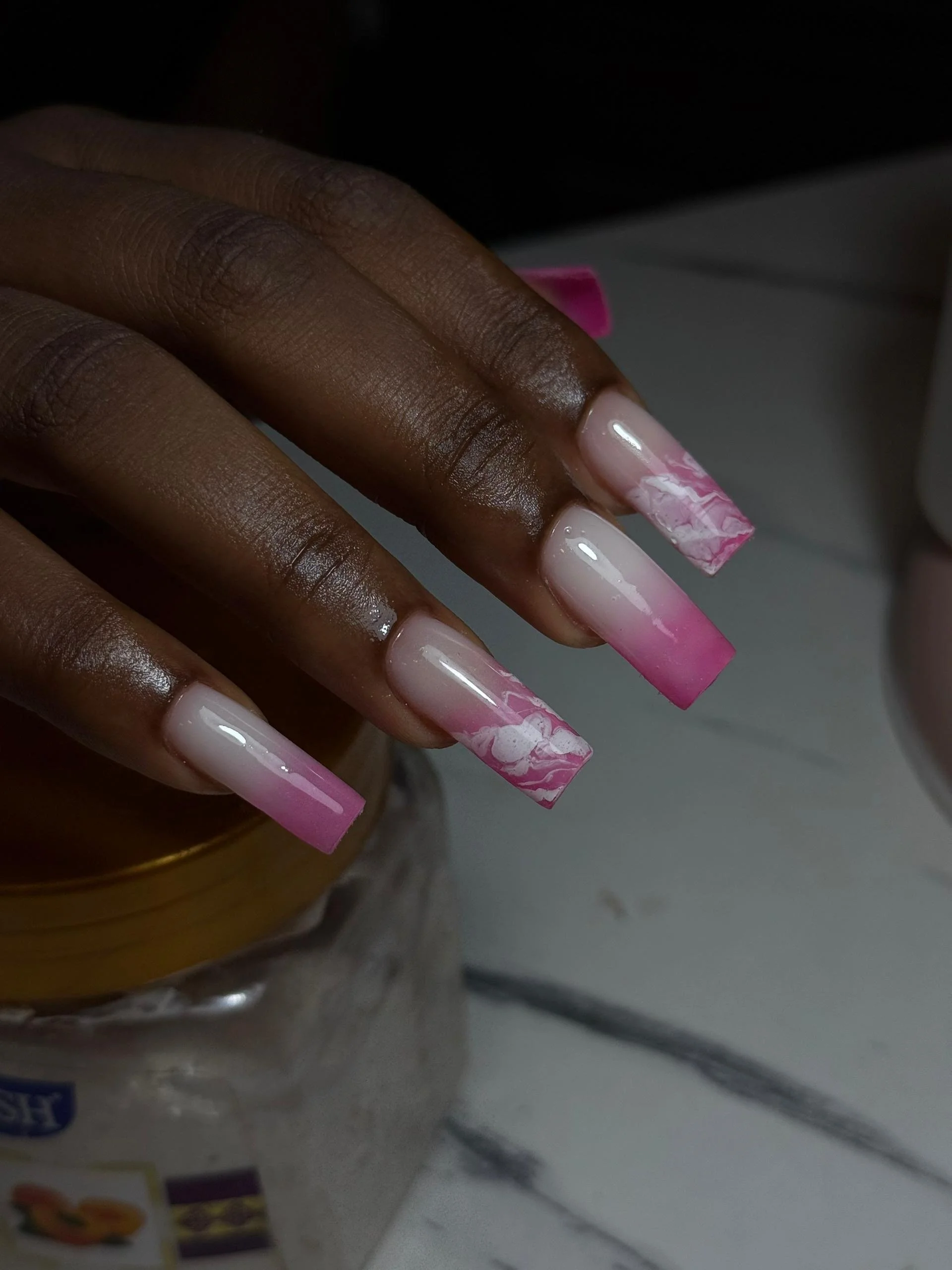Close-up of a hand with long square-shaped nails painted in pink and white marble design.