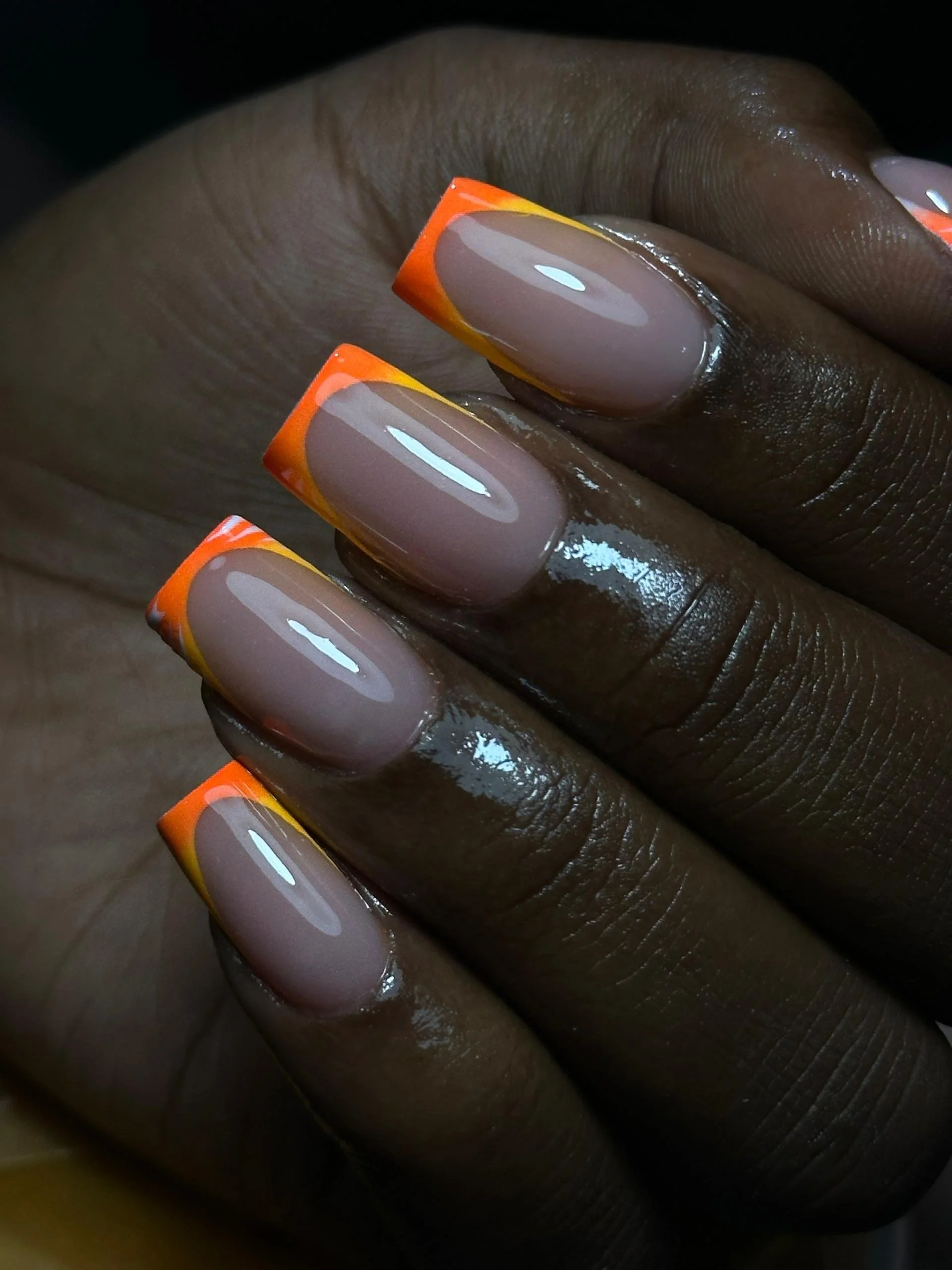 Close-up of a hand with neatly manicured nails featuring a French manicure with bright orange and yellow tips.
